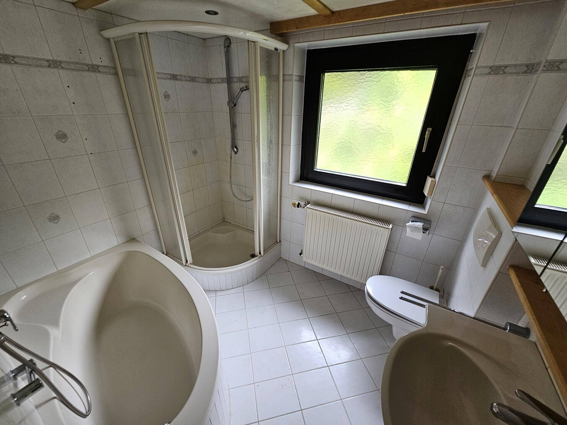 Badezimmer mit Eckbadewanne, Duschkabine und Fenster, in einem älteren Stil.