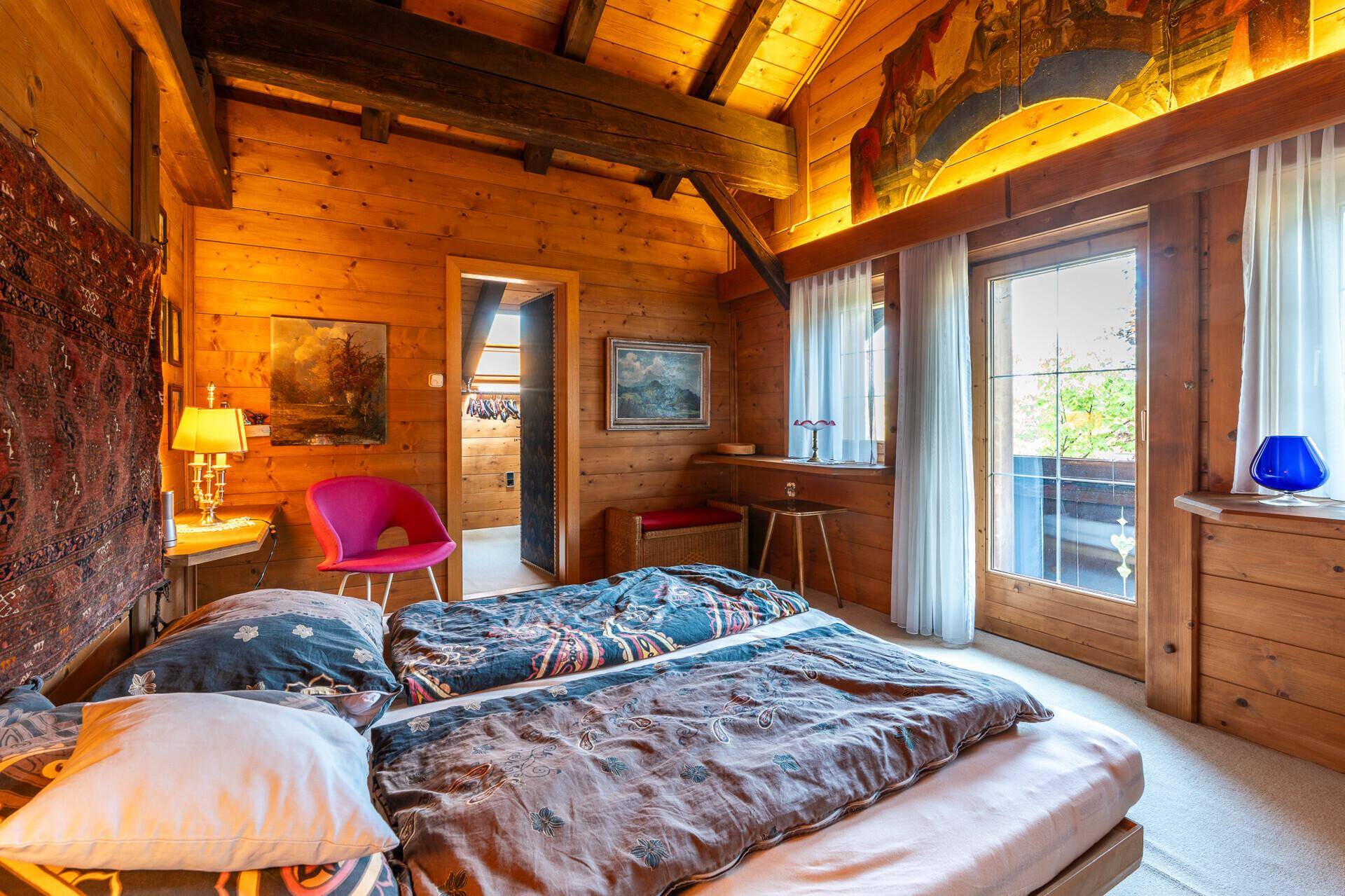 Schlafzimmer mit Holztäfelung an Wänden und Decke, Doppelbett und Zugang zu einem Balkon.
