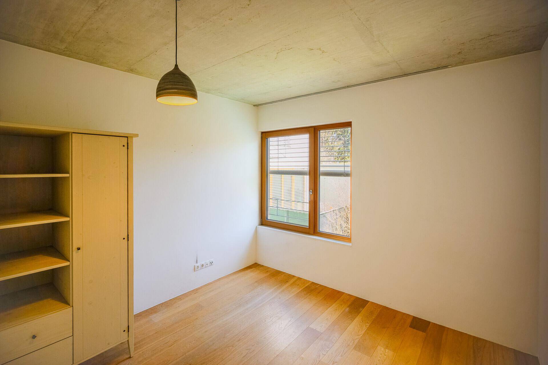 Helles Schlafzimmer mit Holzboden, weiß gestrichenen Wänden und einem Fenster mit Blick ins Grüne.