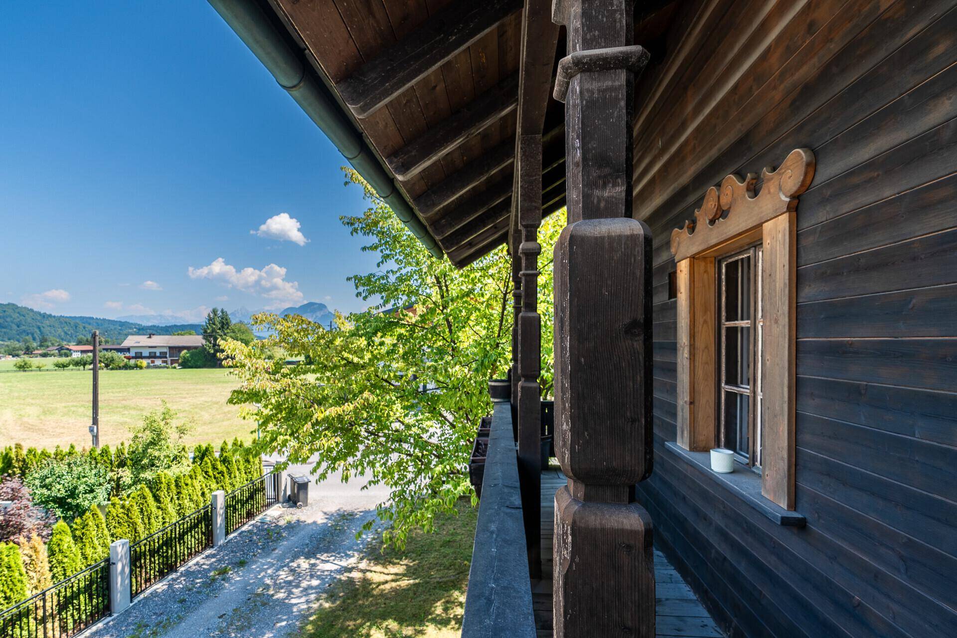 Traditioneller Holzbalkon mit Blick auf grüne Felder und die umliegende Berglandschaft.
