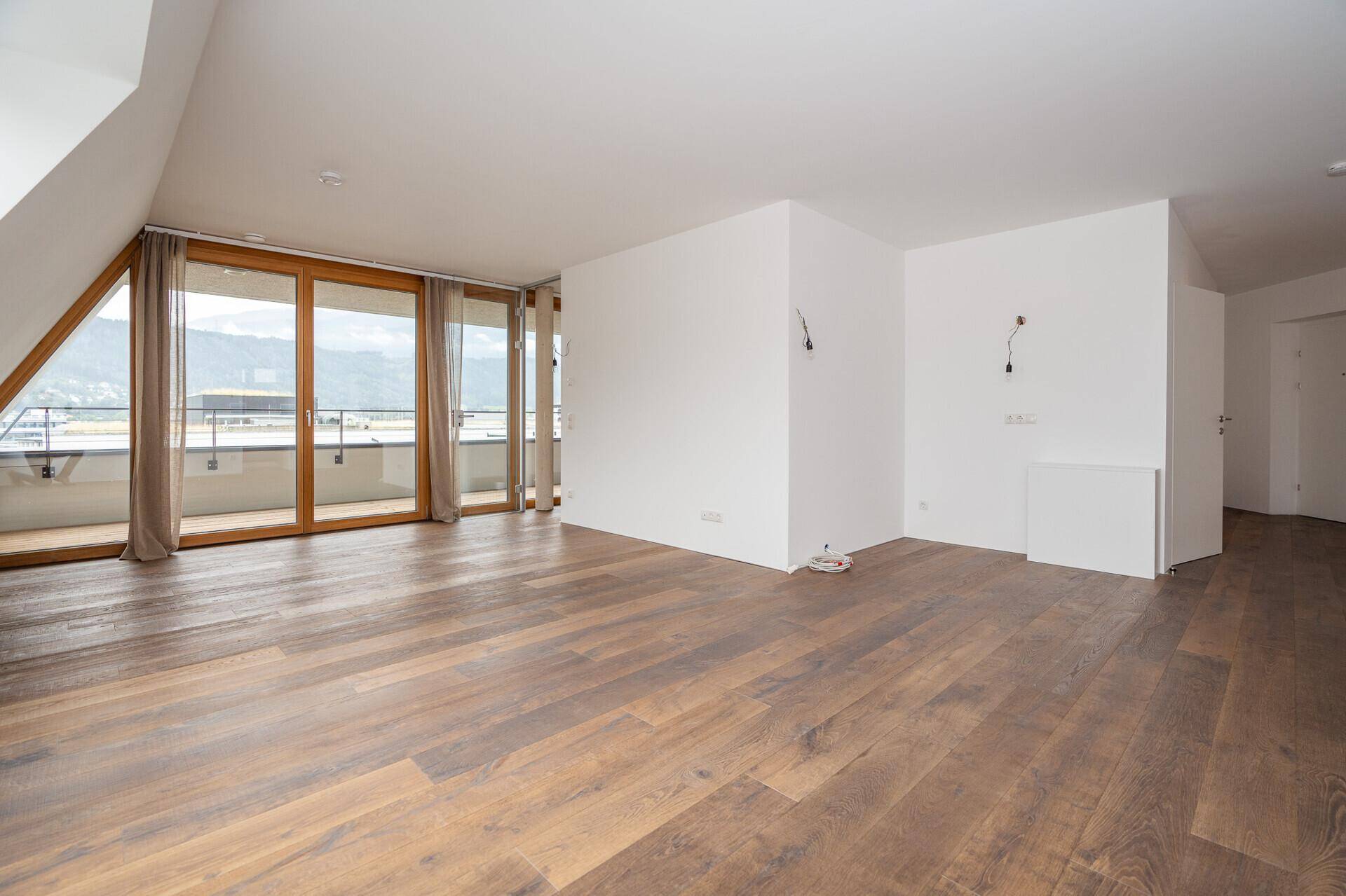 Geräumiger, heller Raum mit Holzboden und großen Balkontüren, die einen weiten Blick bieten.
