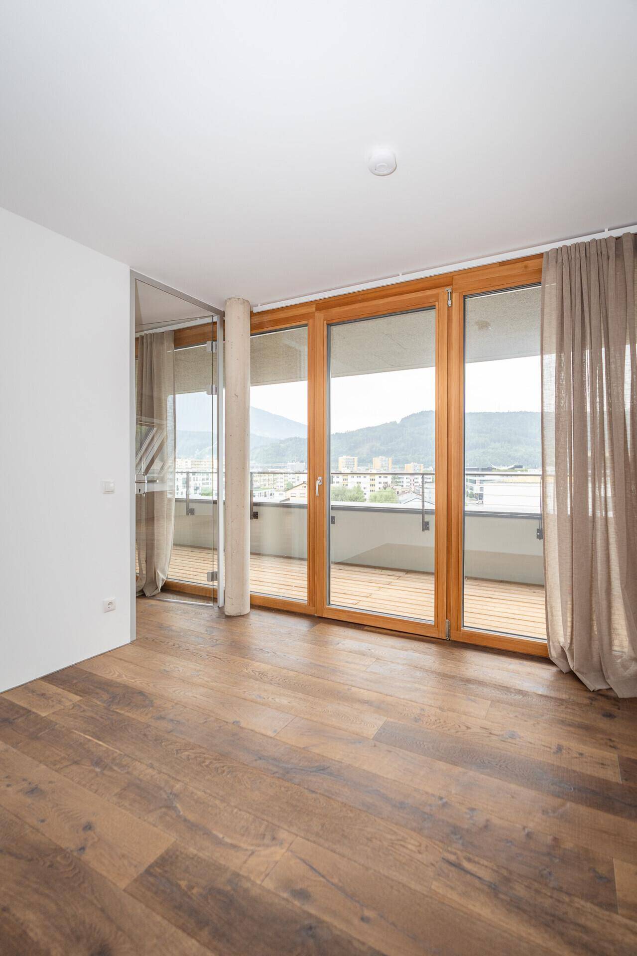 Heller Raum mit Holzboden und großen Balkontüren, die einen weiten Bergblick ermöglichen.