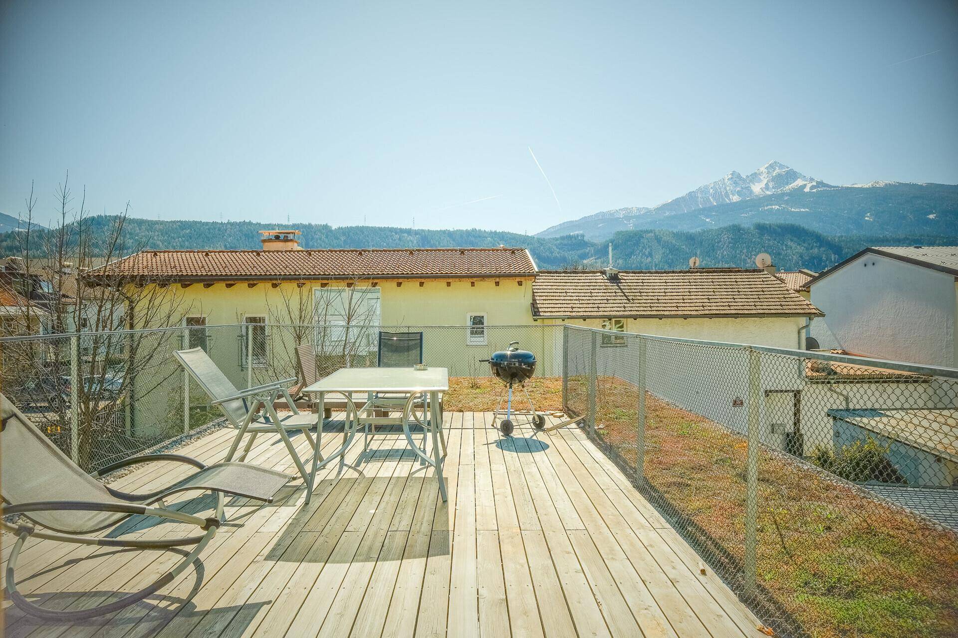 Geräumige Dachterrasse mit Holzboden, Grillplatz und Panoramablick auf die umliegende Berglandschaft.