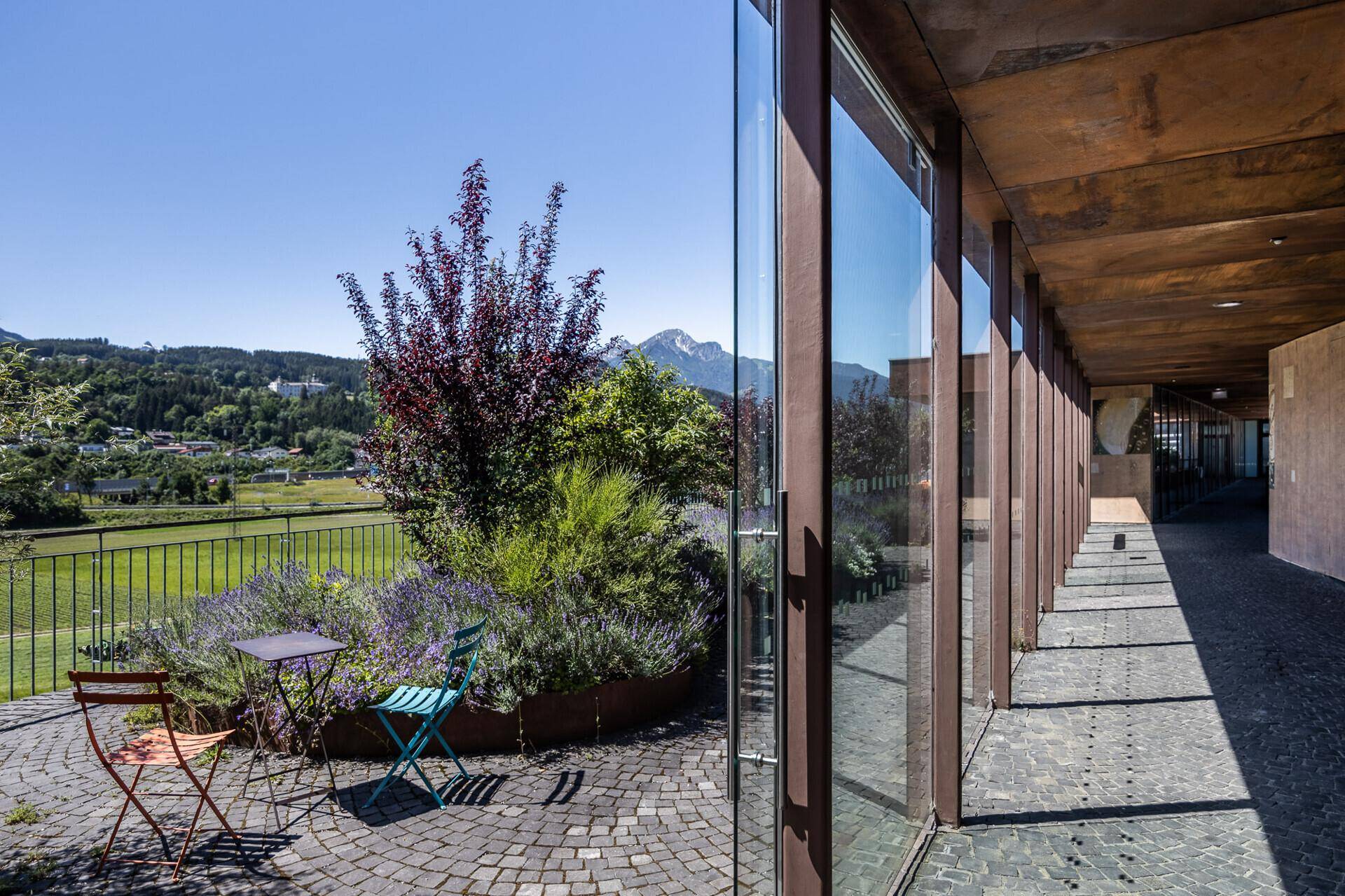 Sonniger Terrassenbereich mit Sitzgelegenheiten, Pflanzen und einem weiten Blick auf die Berge.