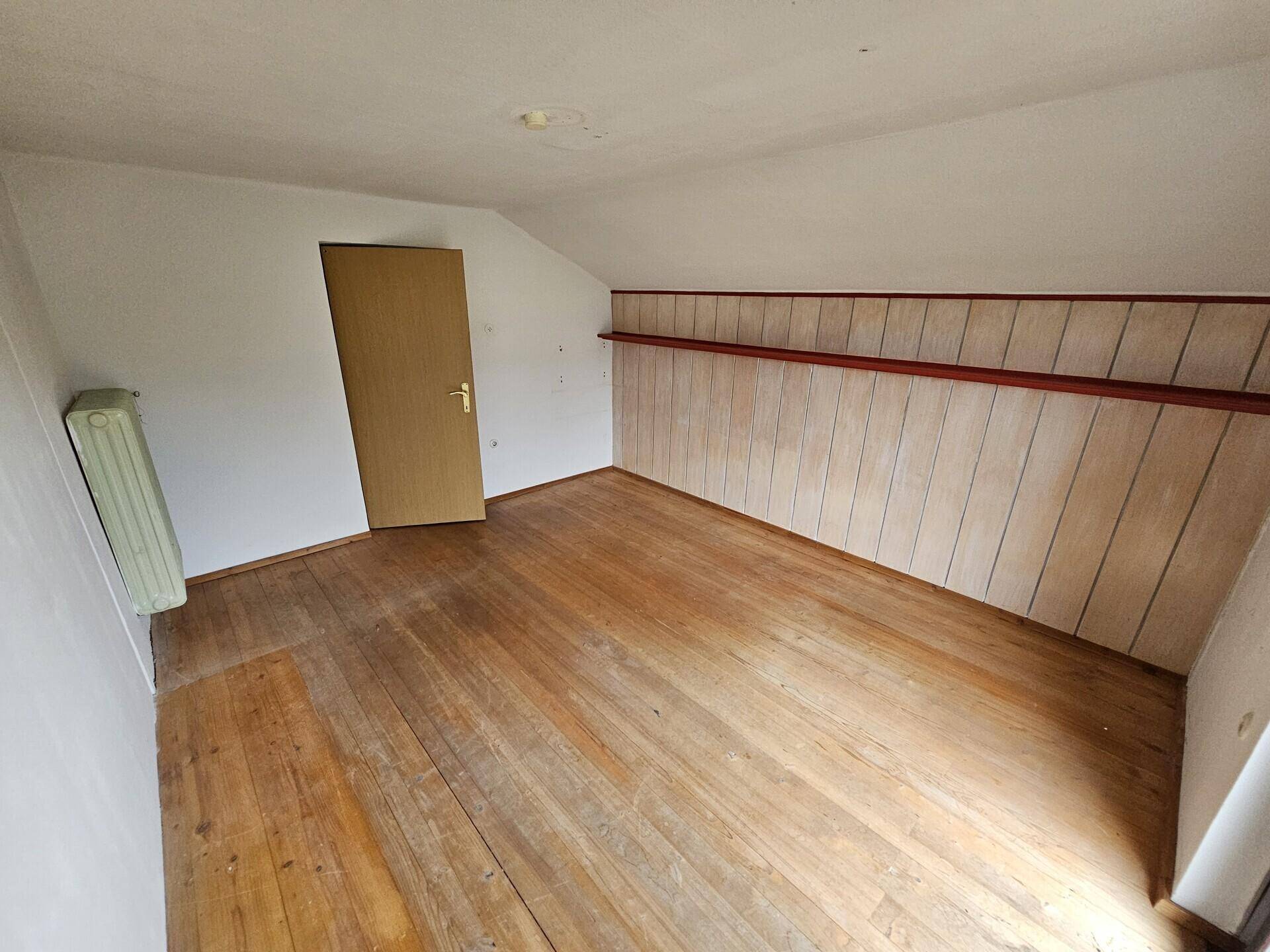 Dachzimmer mit Holzfußboden und schrägen Wänden, bereit zur Renovierung.