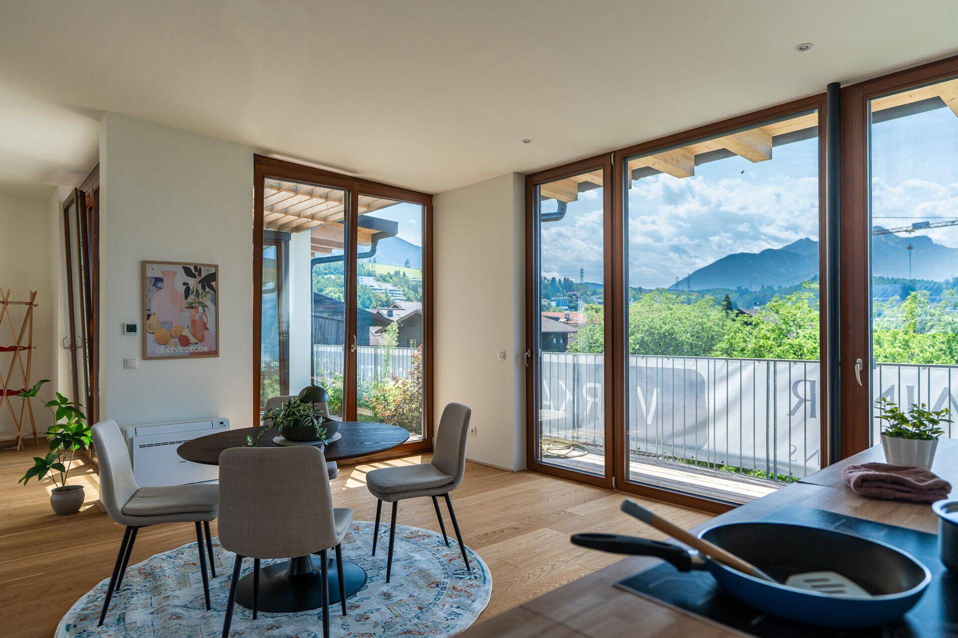 Essbereich mit Holzboden und Blick auf die grüne Umgebung durch große Fenster.