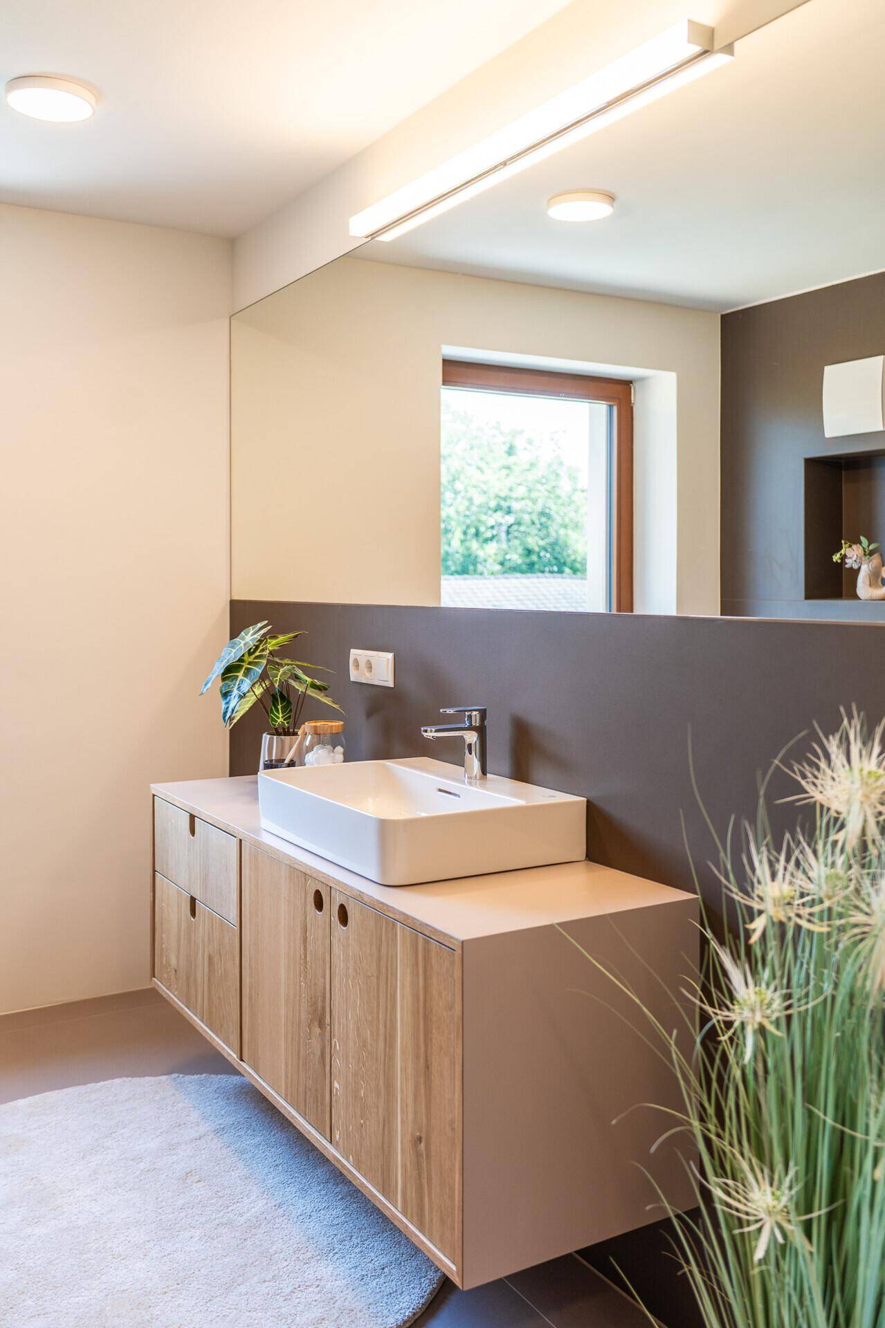 Elegantes Badezimmer mit großem Spiegel, Holzunterschrank und modernem Aufsatzwaschbecken, gut beleuchtet.