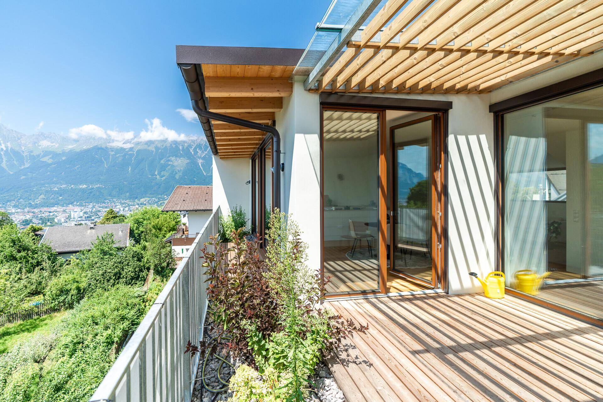 Sonnige Holzterrasse mit Pflanzen, Pergola und weitem Panoramablick auf die Berge.