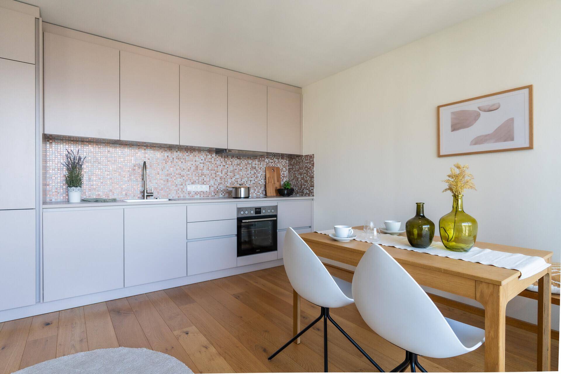 Moderne Küche mit hellen Schränken, Mosaik-Rückwand und Essbereich mit Holztisch.