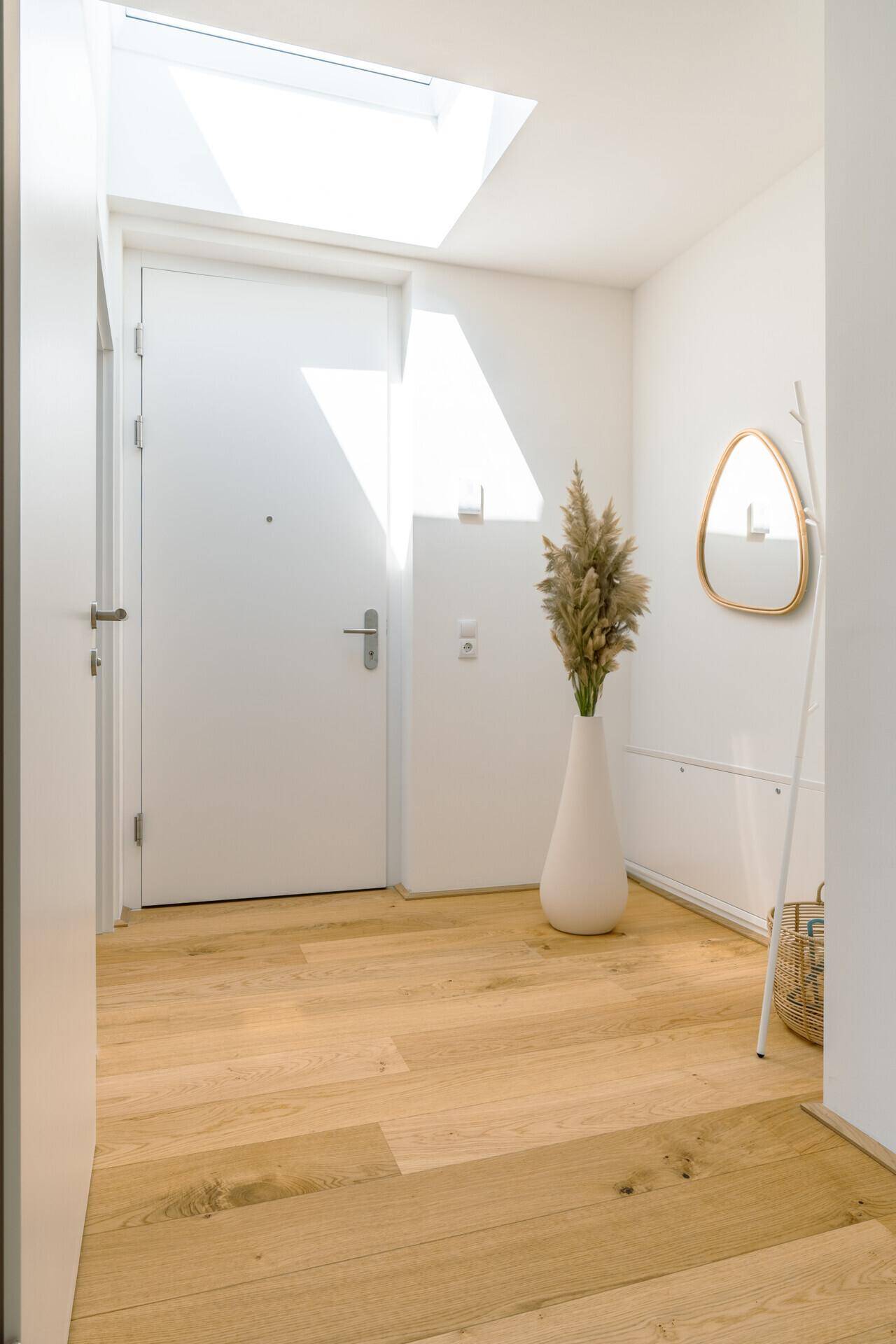Heller Eingangsbereich mit Holzboden, weißer Tür und natürlichem Licht durch ein Oberlicht.