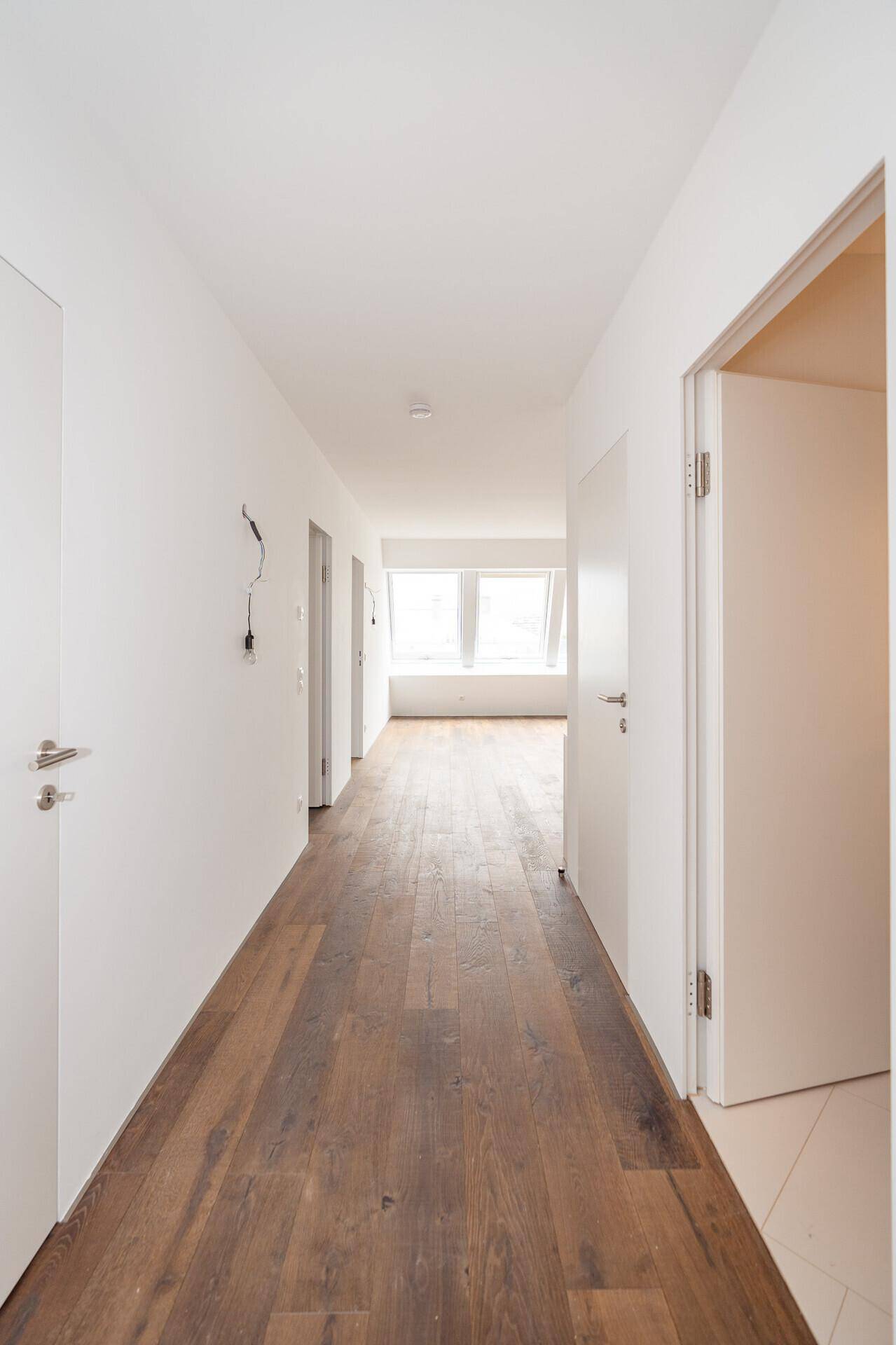 Langer, heller Flur mit Holzboden und weißen Wänden, der zu weiteren Räumen führt.