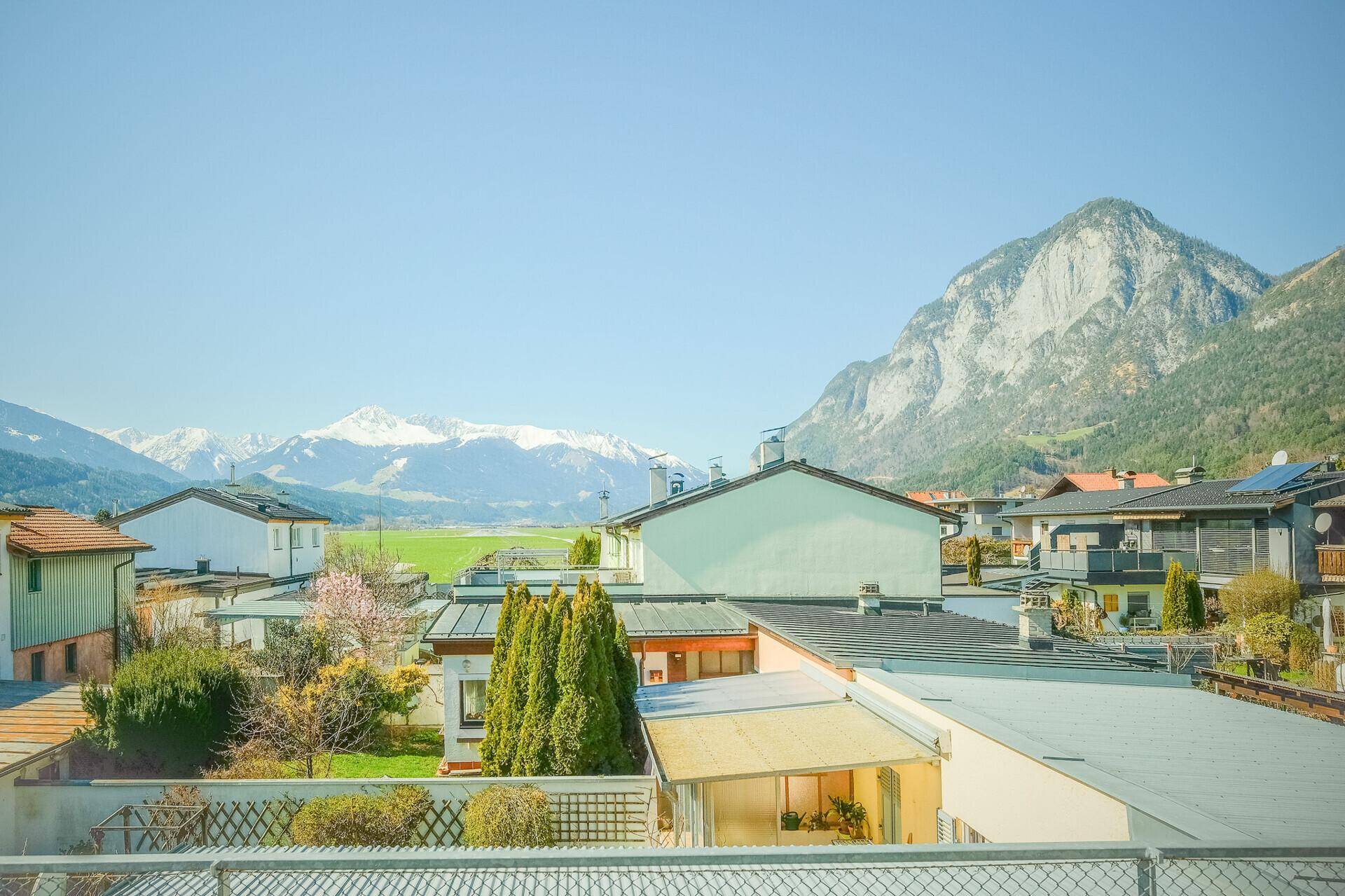 Weitblick über eine Wohnsiedlung mit grünen Feldern und schneebedeckten Bergen im Hintergrund.