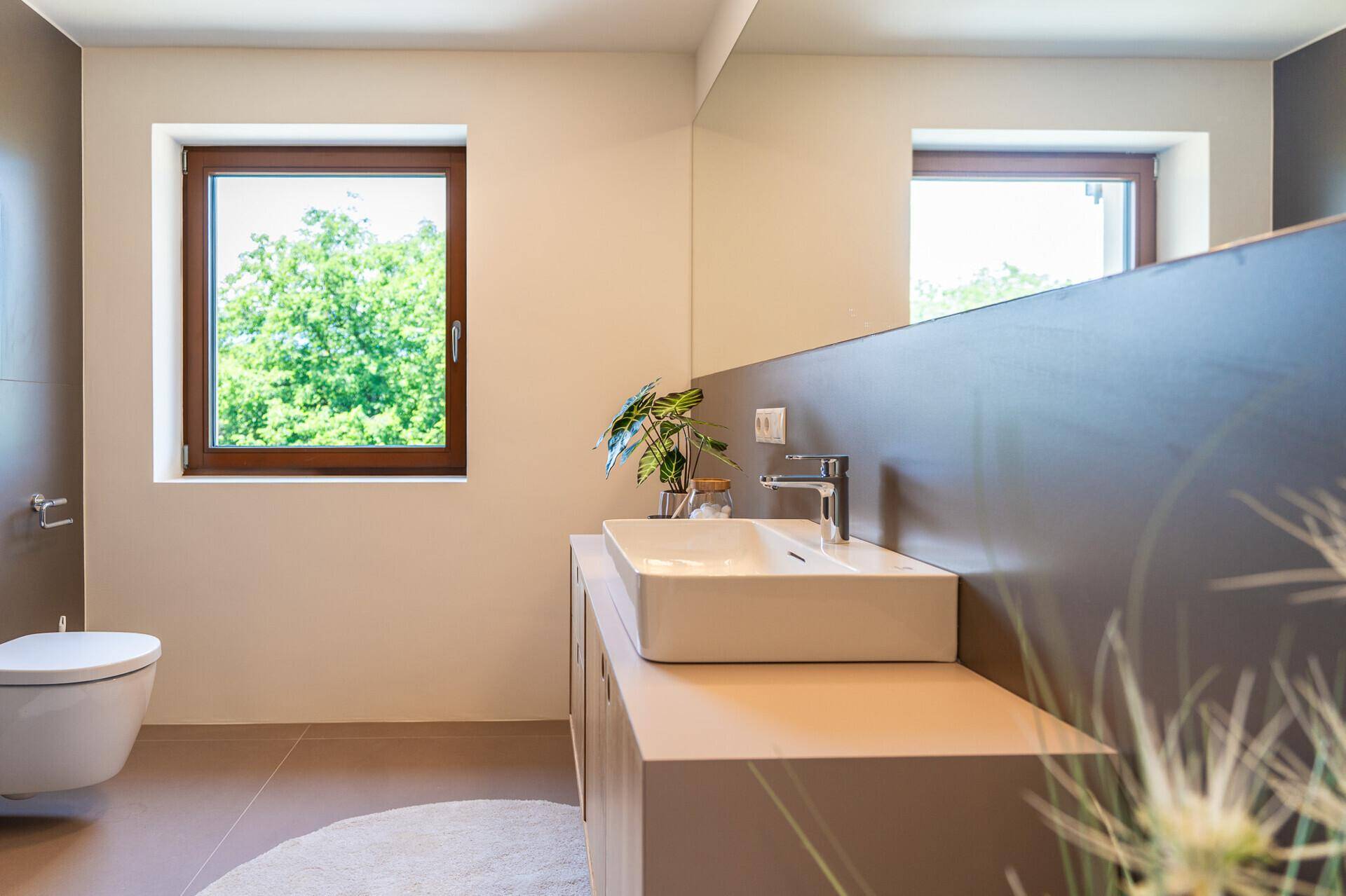 Modernes Badezimmer mit Waschtisch, Wand-WC und Fenster mit Blick ins Grüne.
