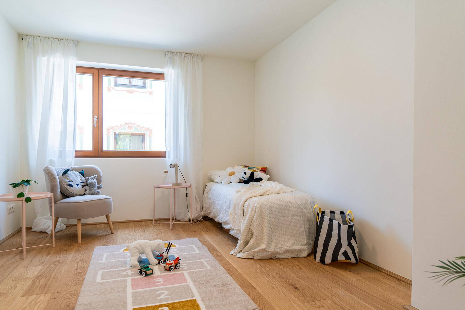 Kinderzimmer mit Holzboden, Einzelbett und einem Fenster, das den Raum hell und freundlich macht.
