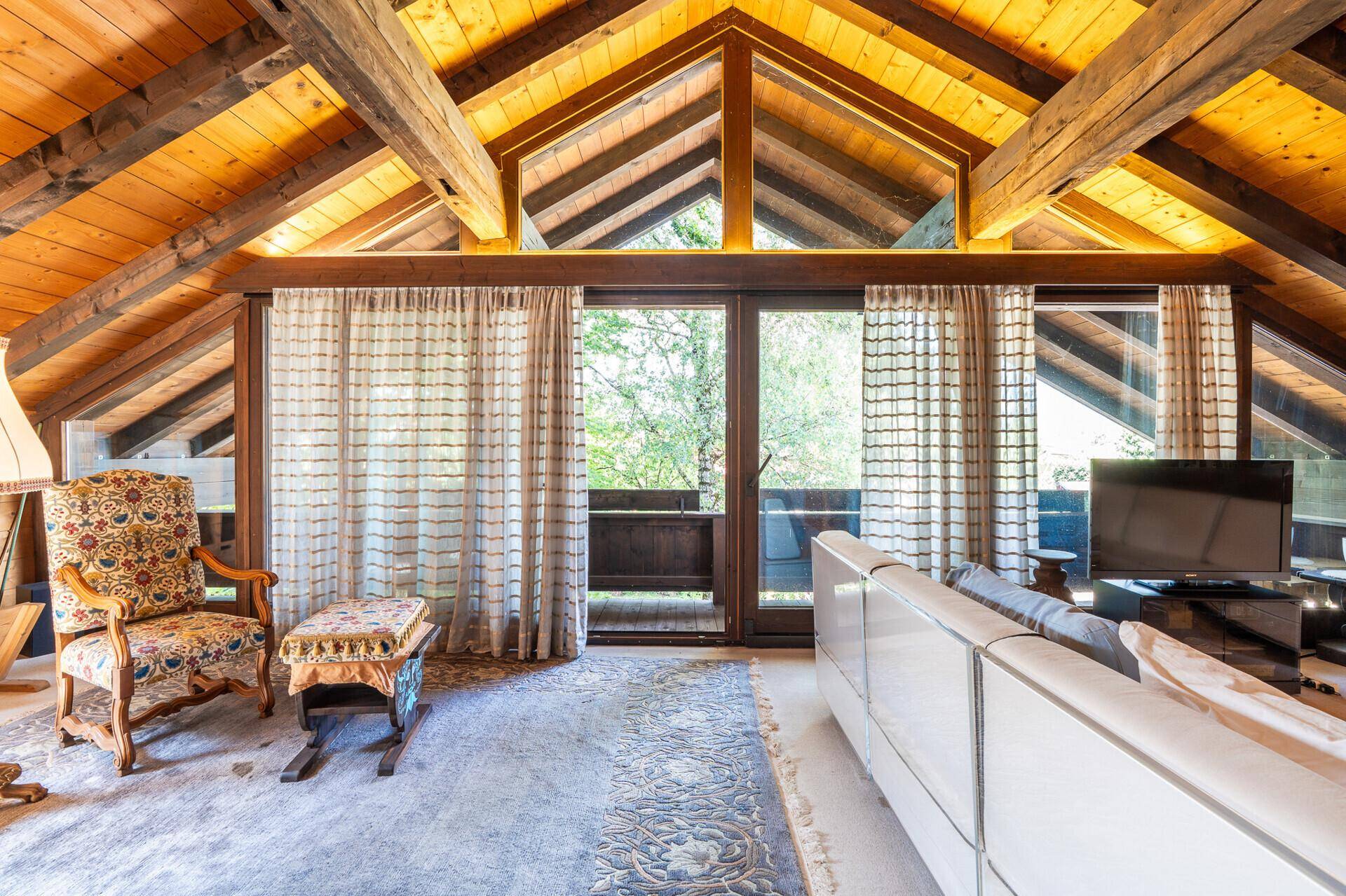 Gemütliches Wohnzimmer im Dachgeschoss mit sichtbaren Holzbalken, hohen Decken und Balkonzugang.
