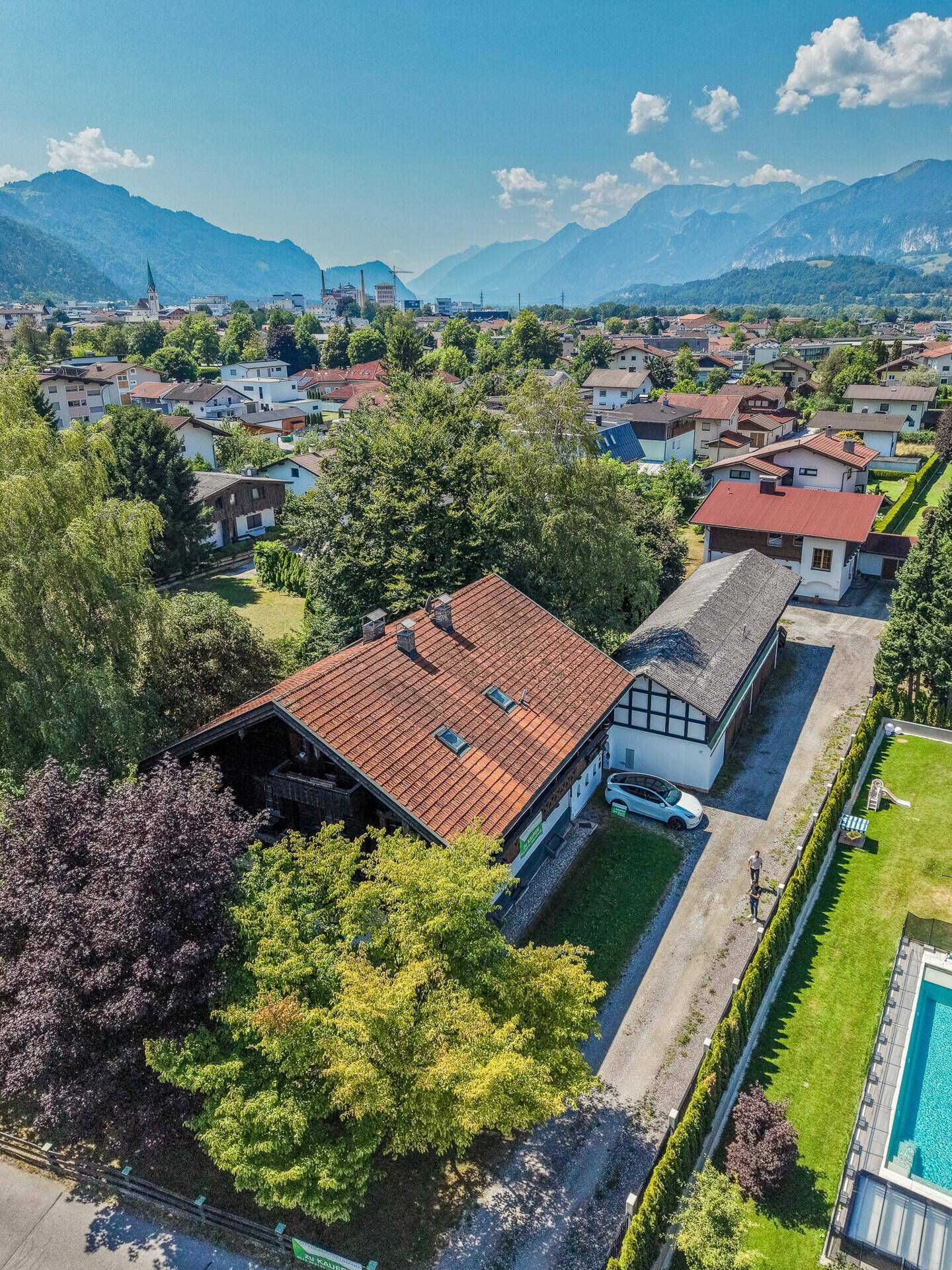 Luftaufnahme des Anwesens mit Hauptgebäude, Nebengebäude und Zufahrt, umgeben von Grünflächen.