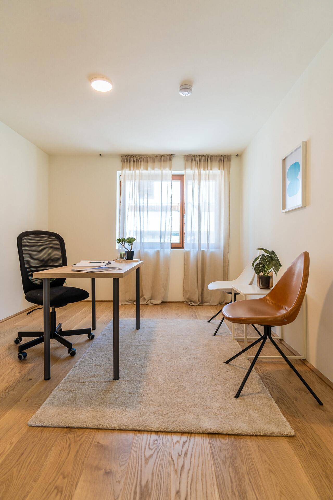Helles Arbeitszimmer mit Holzboden, Schreibtisch und zwei Stühlen.