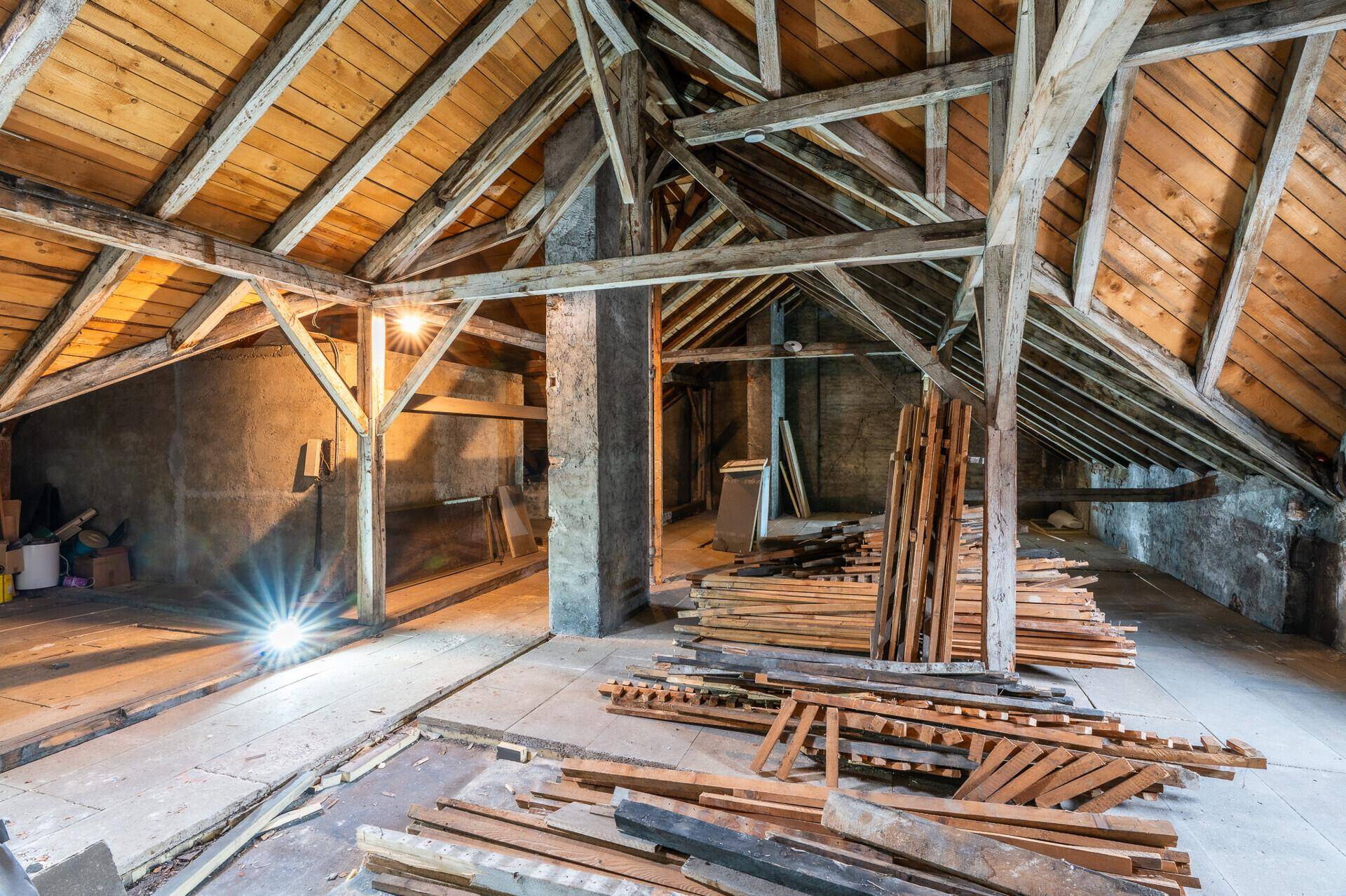 Geräumiger Dachboden mit freiliegenden Holzbalken und Baumaterialien, ideal für einen Ausbau.