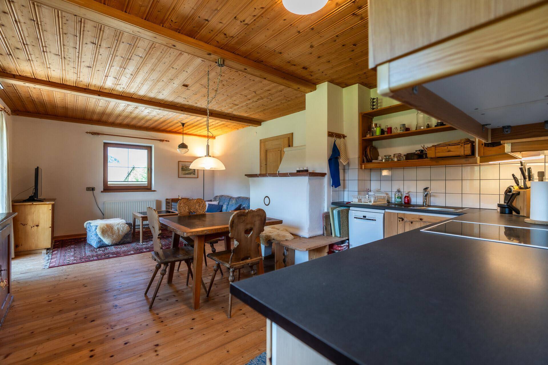 Gemütlicher Wohn-Essbereich mit Holzboden, Holzdecke, traditionellem Kachelofen und offener Küche.