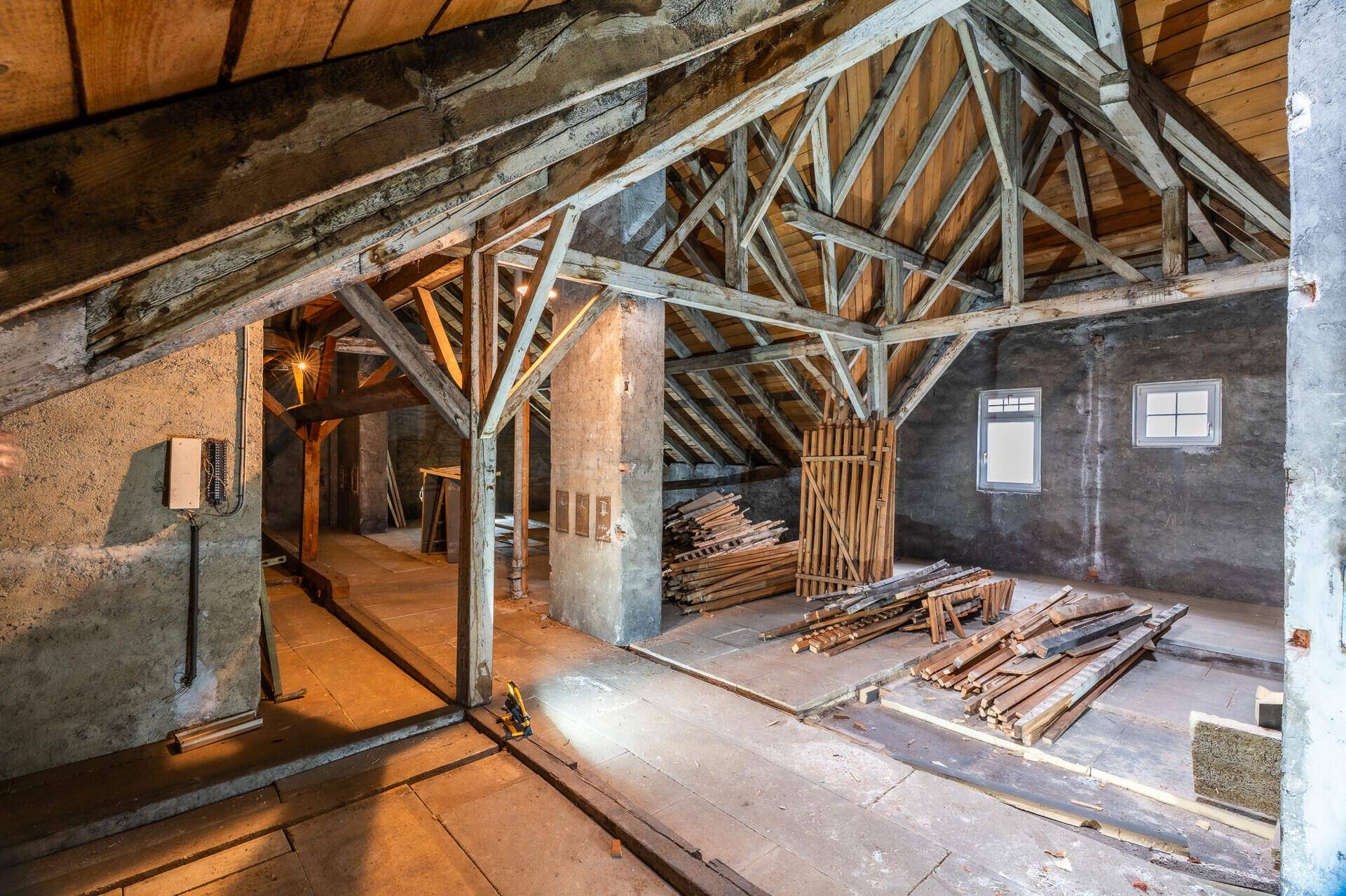 Unfertiger Dachboden mit sichtbarer Holzkonstruktion und Baumaterialien, bereit für den Ausbau.