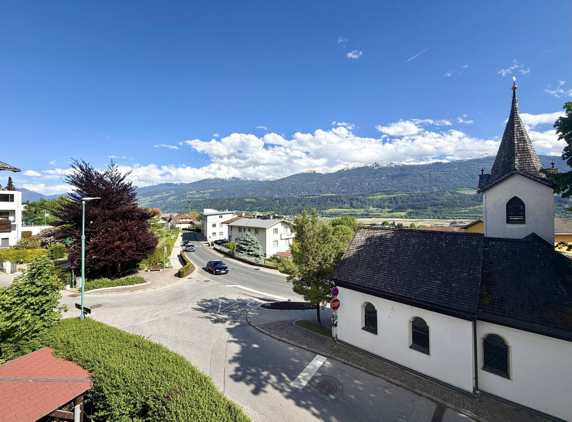 Panoramablick auf die umliegende Landschaft mit Bergen, einer kleinen Kirche und einer Straße.