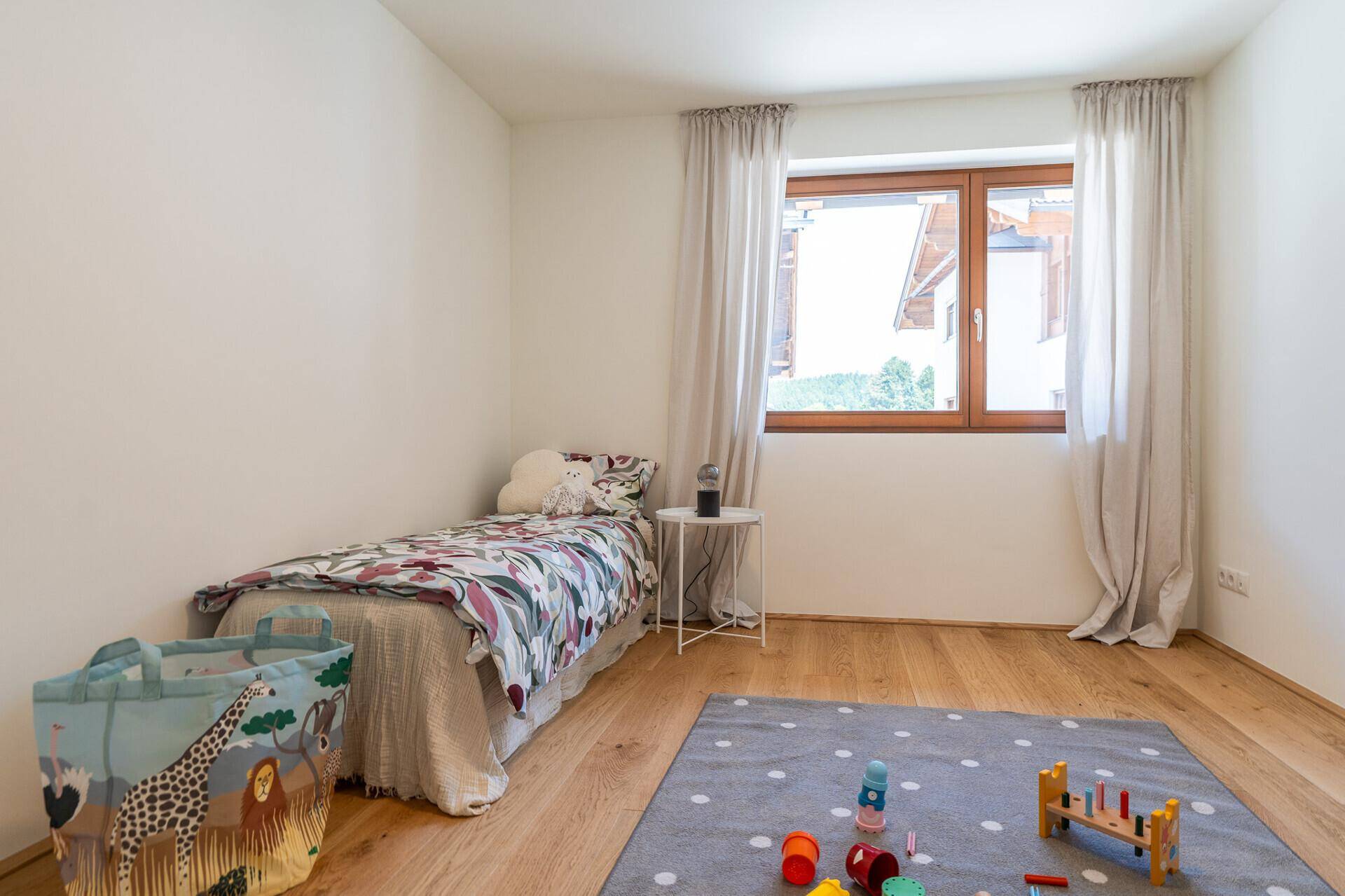 Helles Kinderzimmer mit Holzboden, großem Fenster und Spielzeug, ideal für junge Familien.