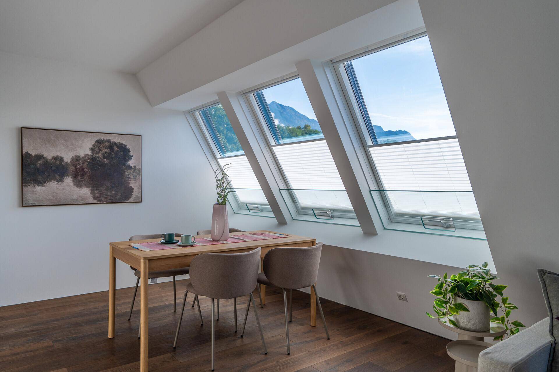 Heller Essbereich mit Holztisch, modernen Stühlen und Dachfenstern mit Bergblick.