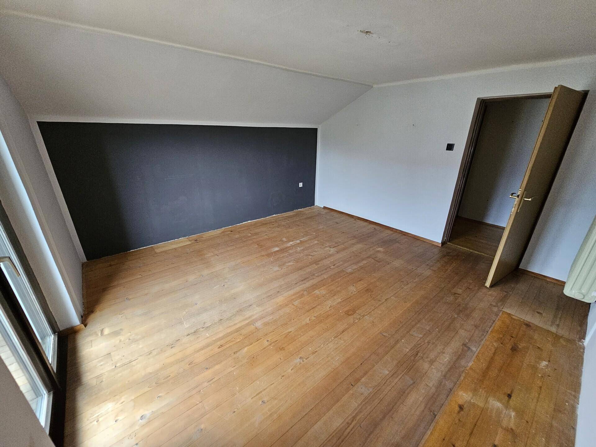 Dachzimmer mit Holzboden, schrägen Wänden und Zugang zum Balkon.