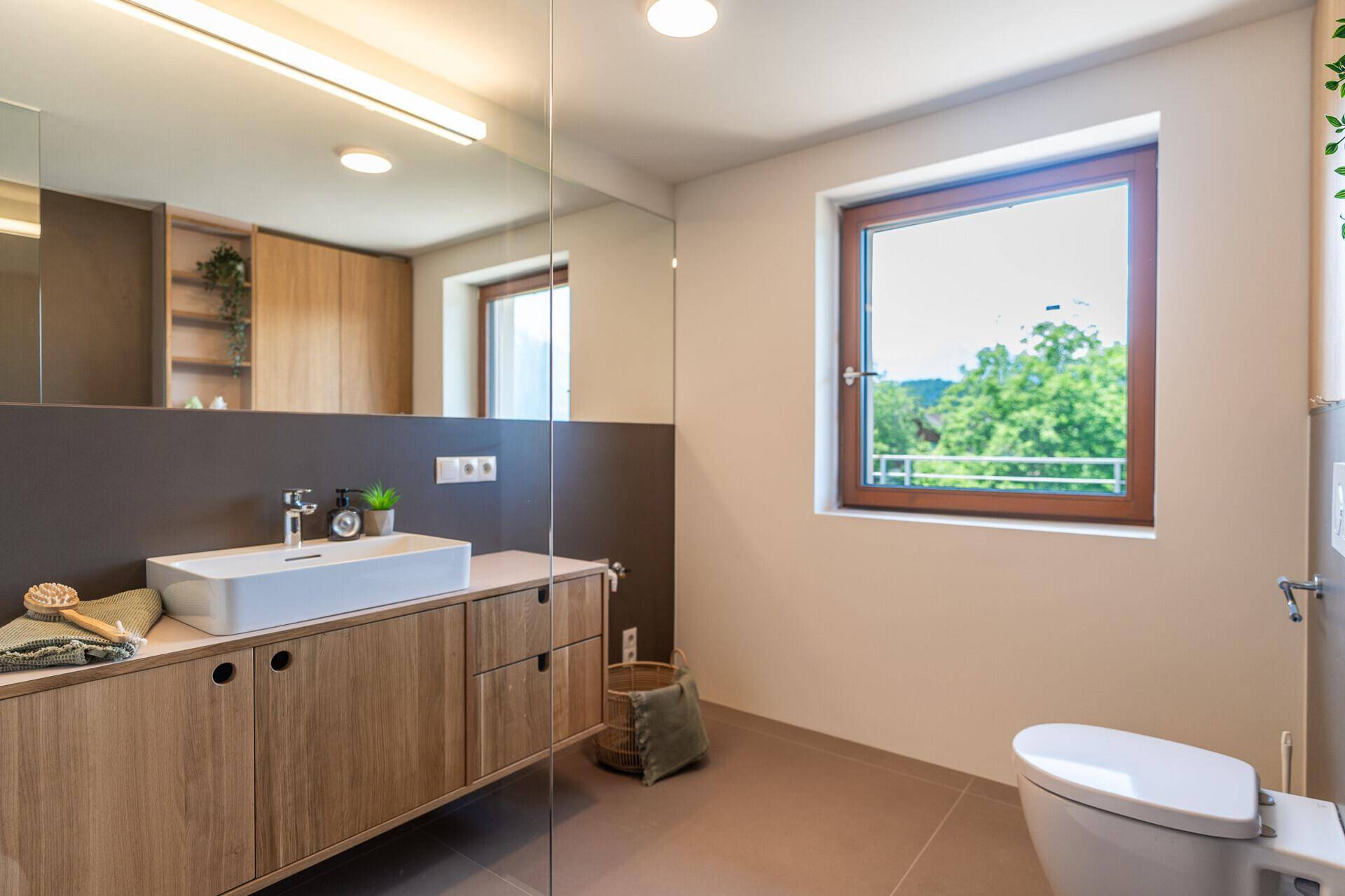 Helles Badezimmer mit Fenster, wandhängendem WC, großem Spiegel und modernem Design.