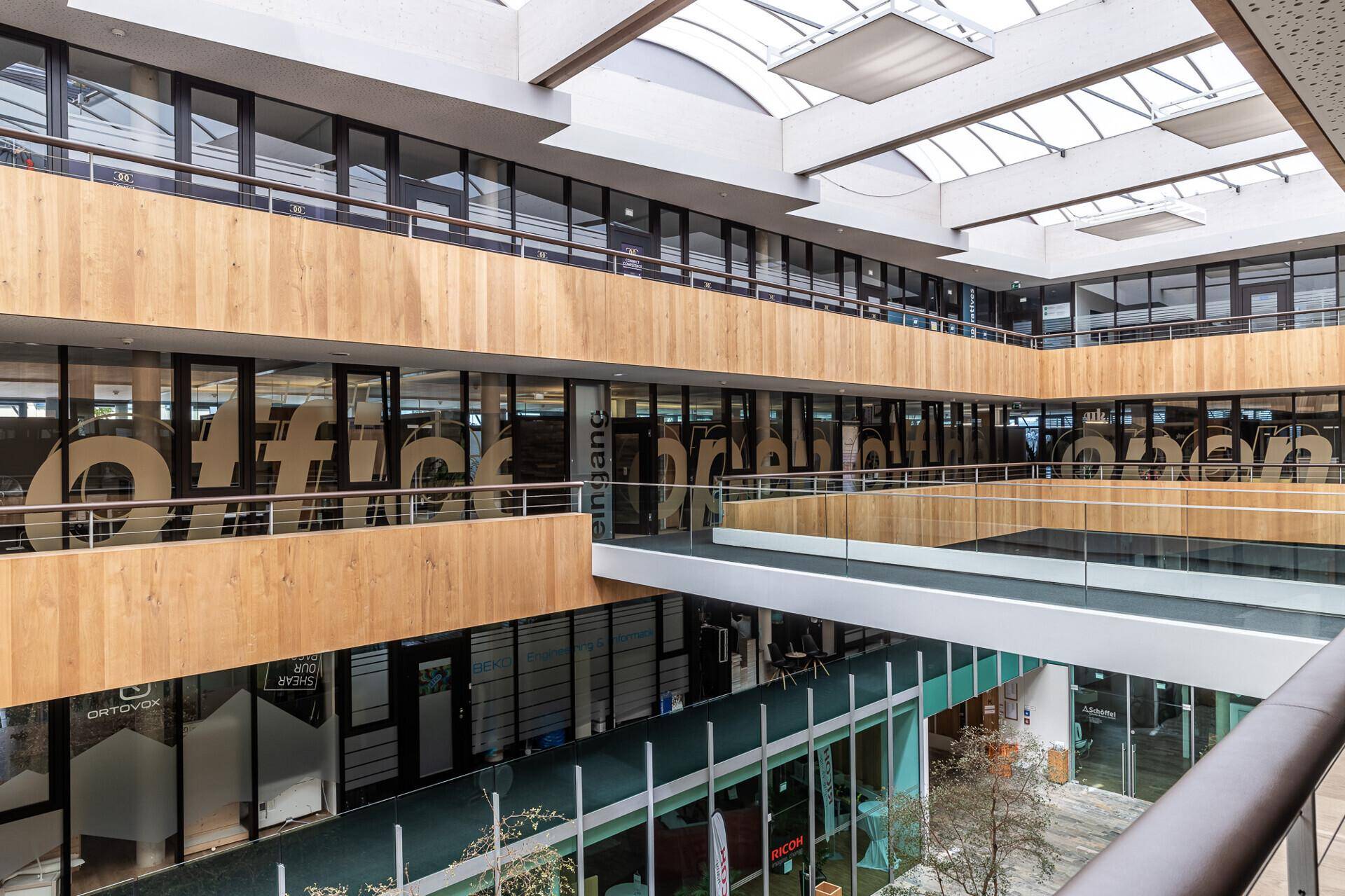 Mehrstöckiges Atrium mit Glasfassaden, Holzverkleidungen und Oberlichtern.