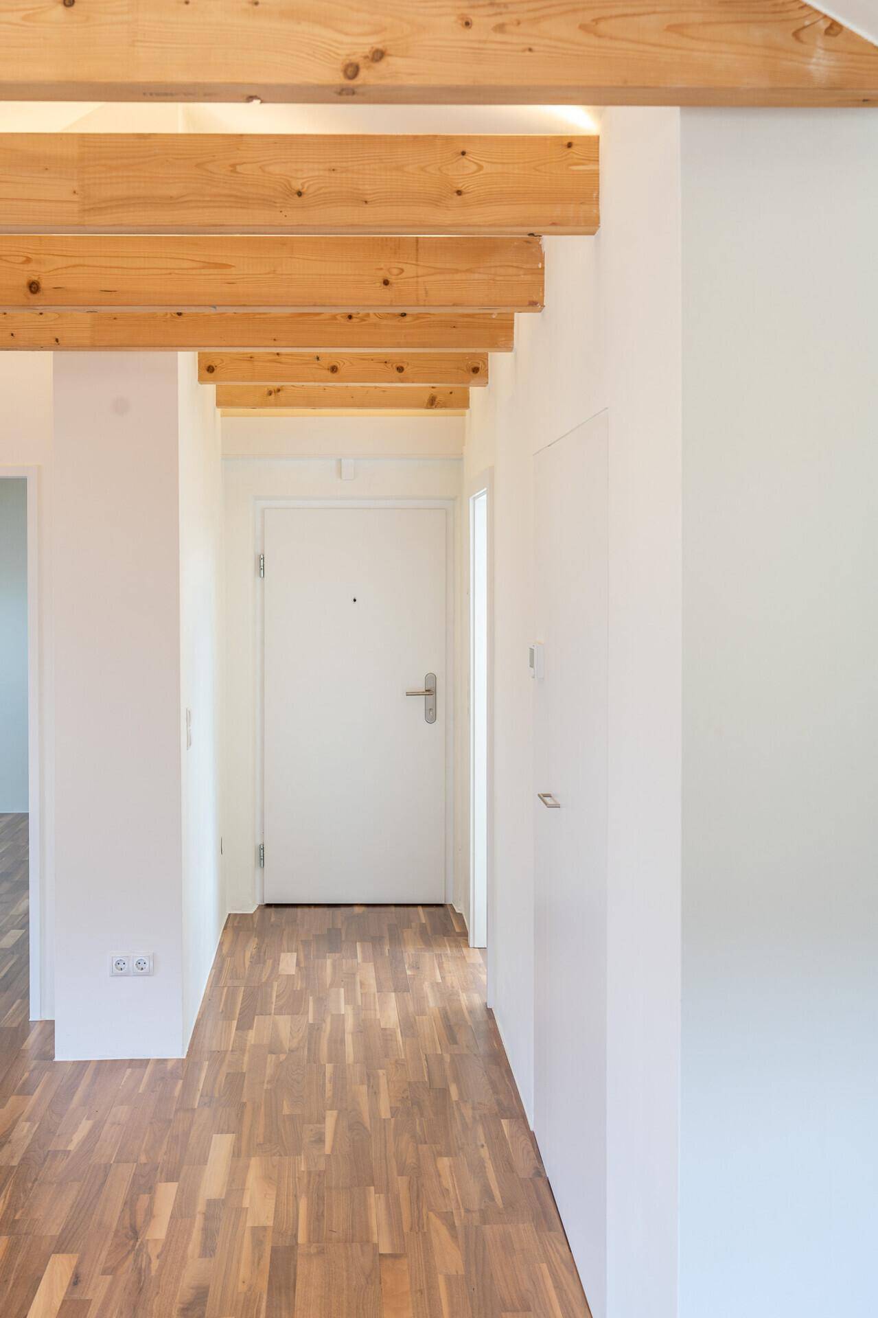 Heller Flur mit Parkettboden, weißer Eingangstür und dekorativen Holzbalken an der Decke.