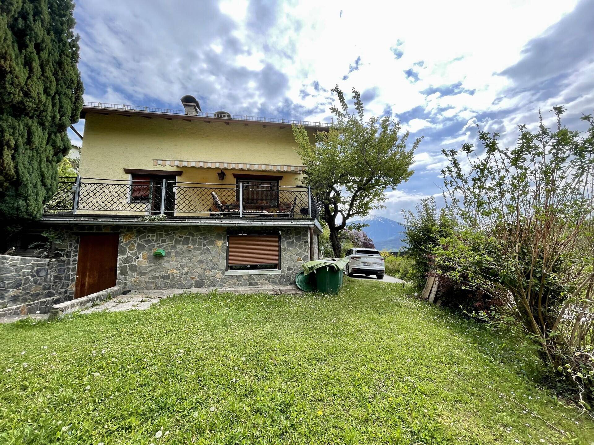 Haus mit großem Garten, Steinfassade und Blick auf die umliegende Natur und Berge.