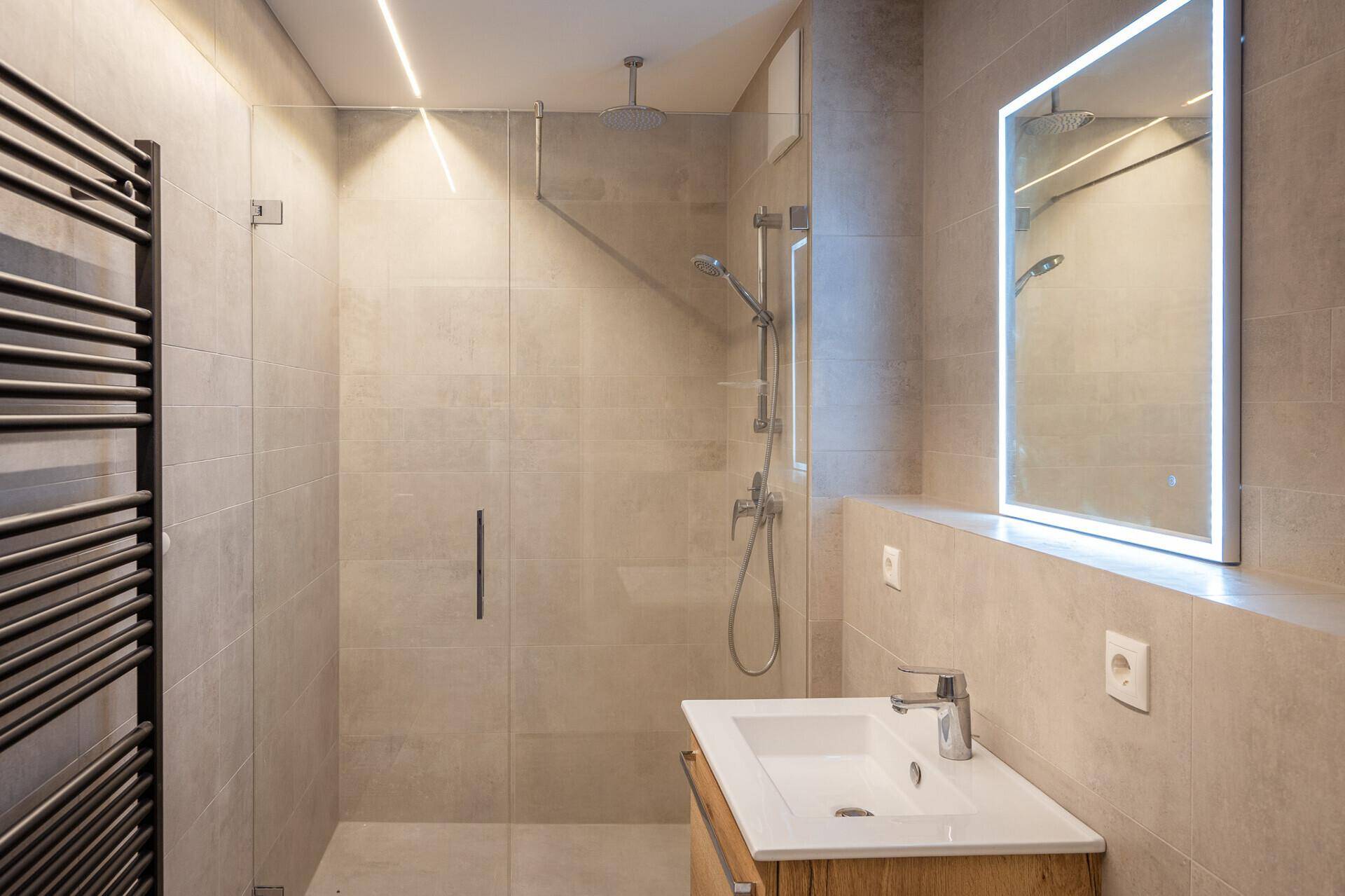 Modernes Badezimmer mit begehbarer Dusche, beheiztem Handtuchhalter und beleuchtetem Spiegel.