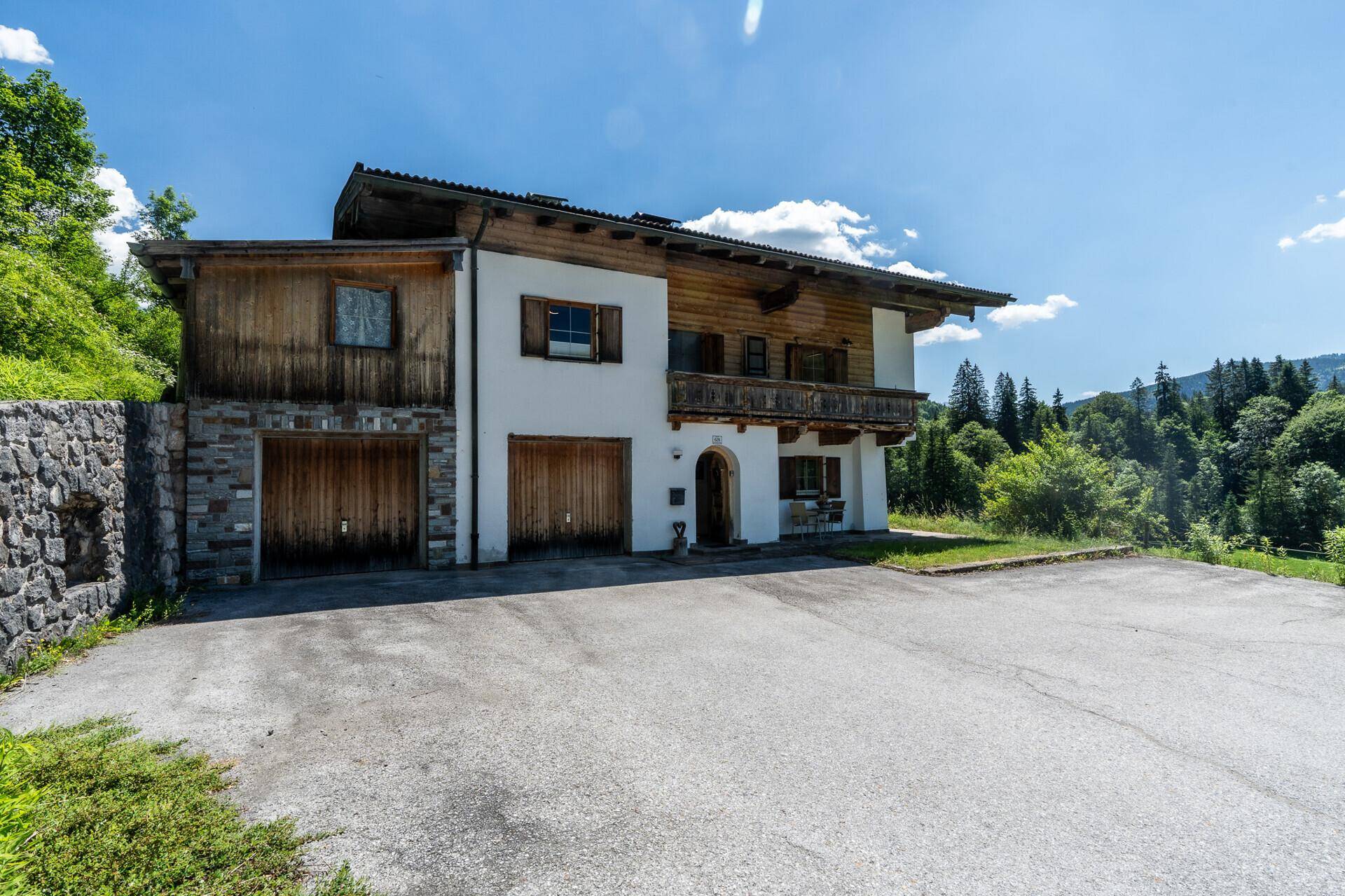 Vorderansicht des Hauses mit Garagen, Steinfassade und traditionellen Holzelementen.