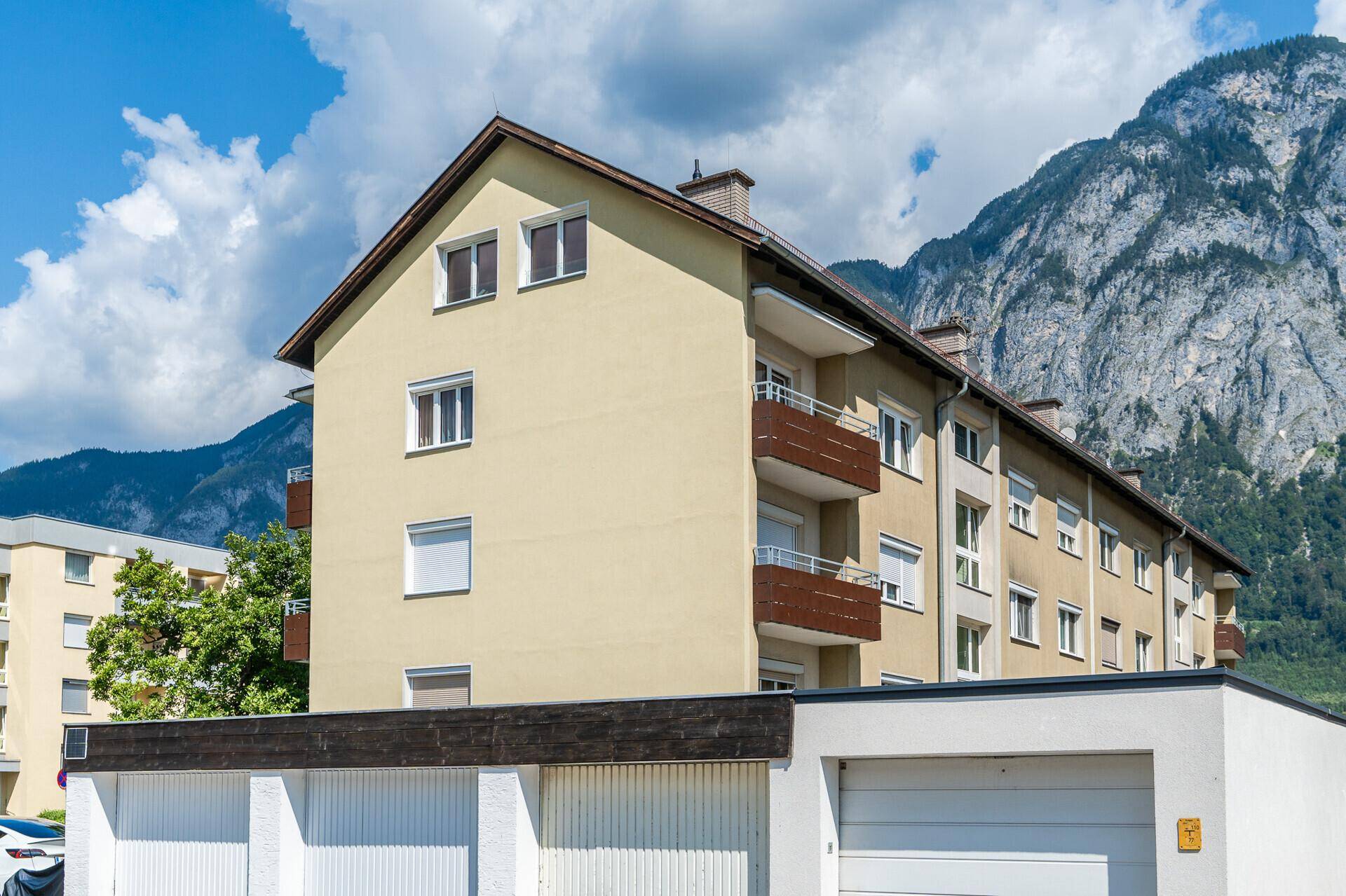 Mehrfamilienhaus mit Balkonen und Garagen im Vordergrund, umgeben von einer beeindruckenden Bergkulisse.