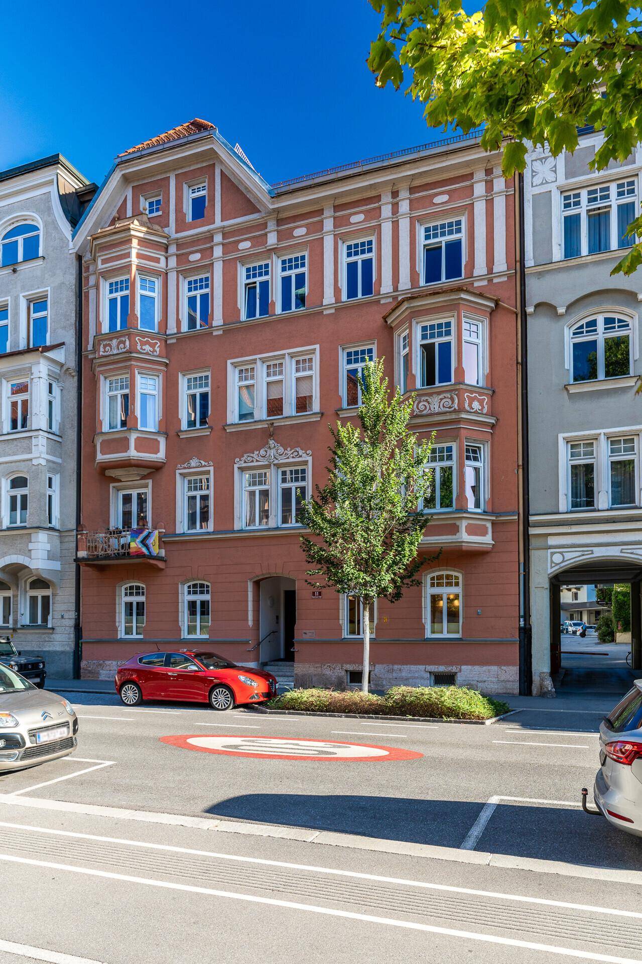 Historische Fassade eines Stadthauses mit Erkern und einem Baum davor an einem sonnigen Tag.