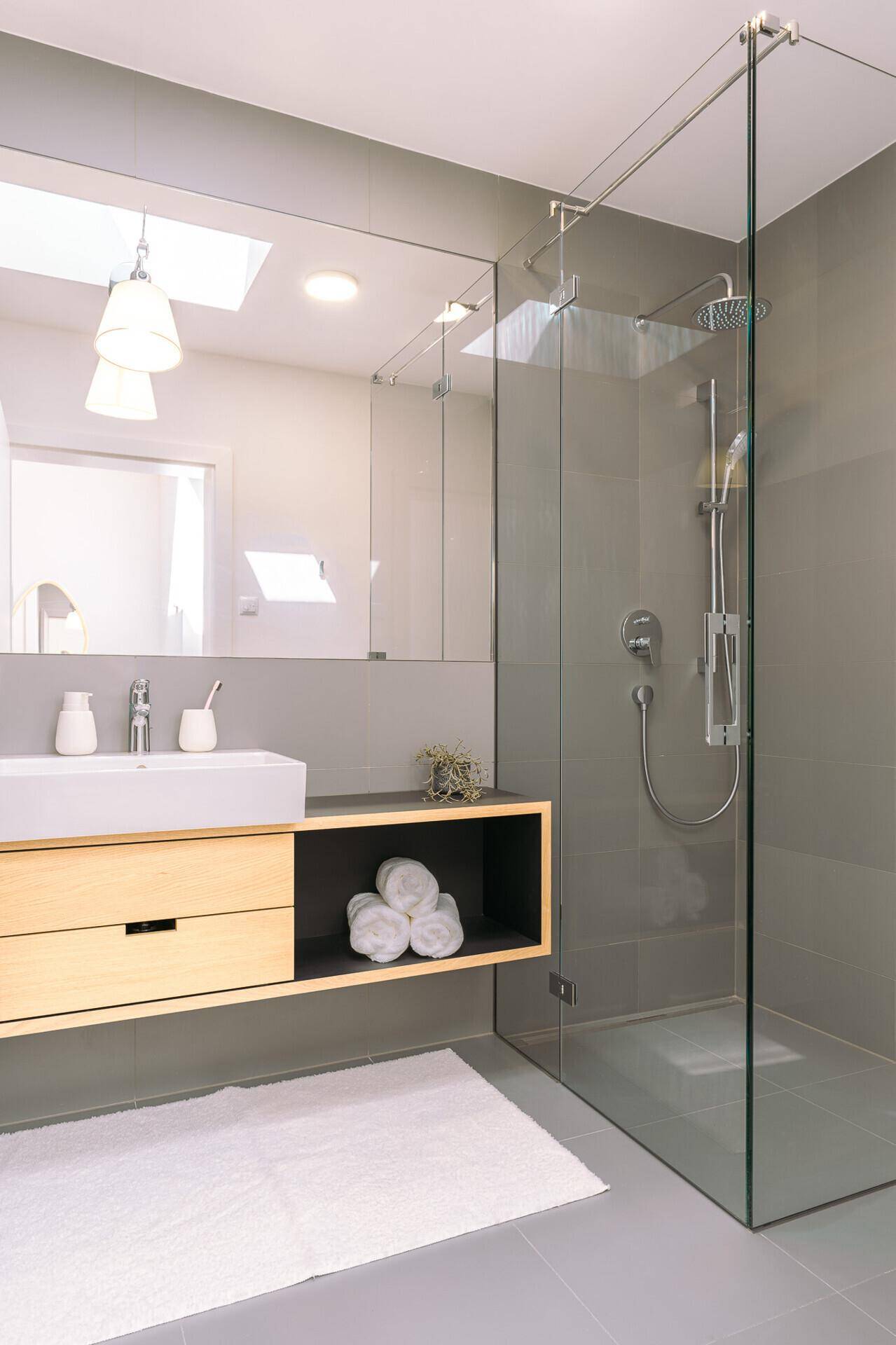 Modernes Badezimmer mit begehbarer Dusche, Einzelwaschbecken und großen grauen Fliesen.