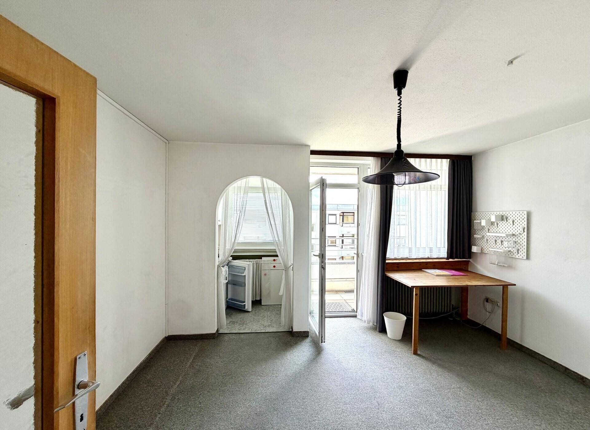 Heller Wohnraum mit Zugang zum Balkon und einer kleinen Küchennische im Bogen.