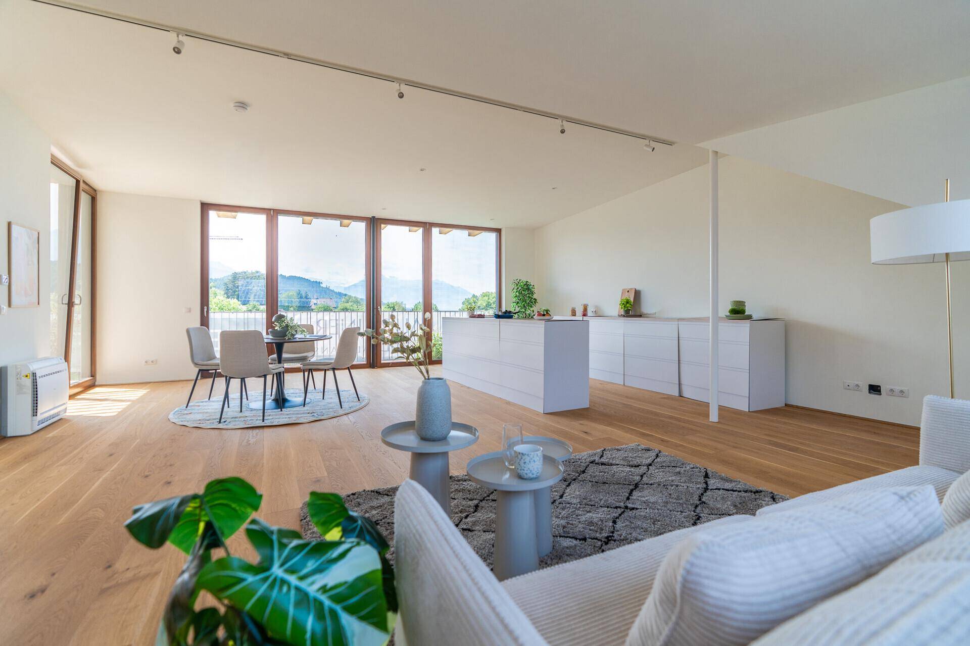 Heller, offener Wohn-Essbereich mit moderner Küche, Holzboden und großen Fenstern mit Bergblick.