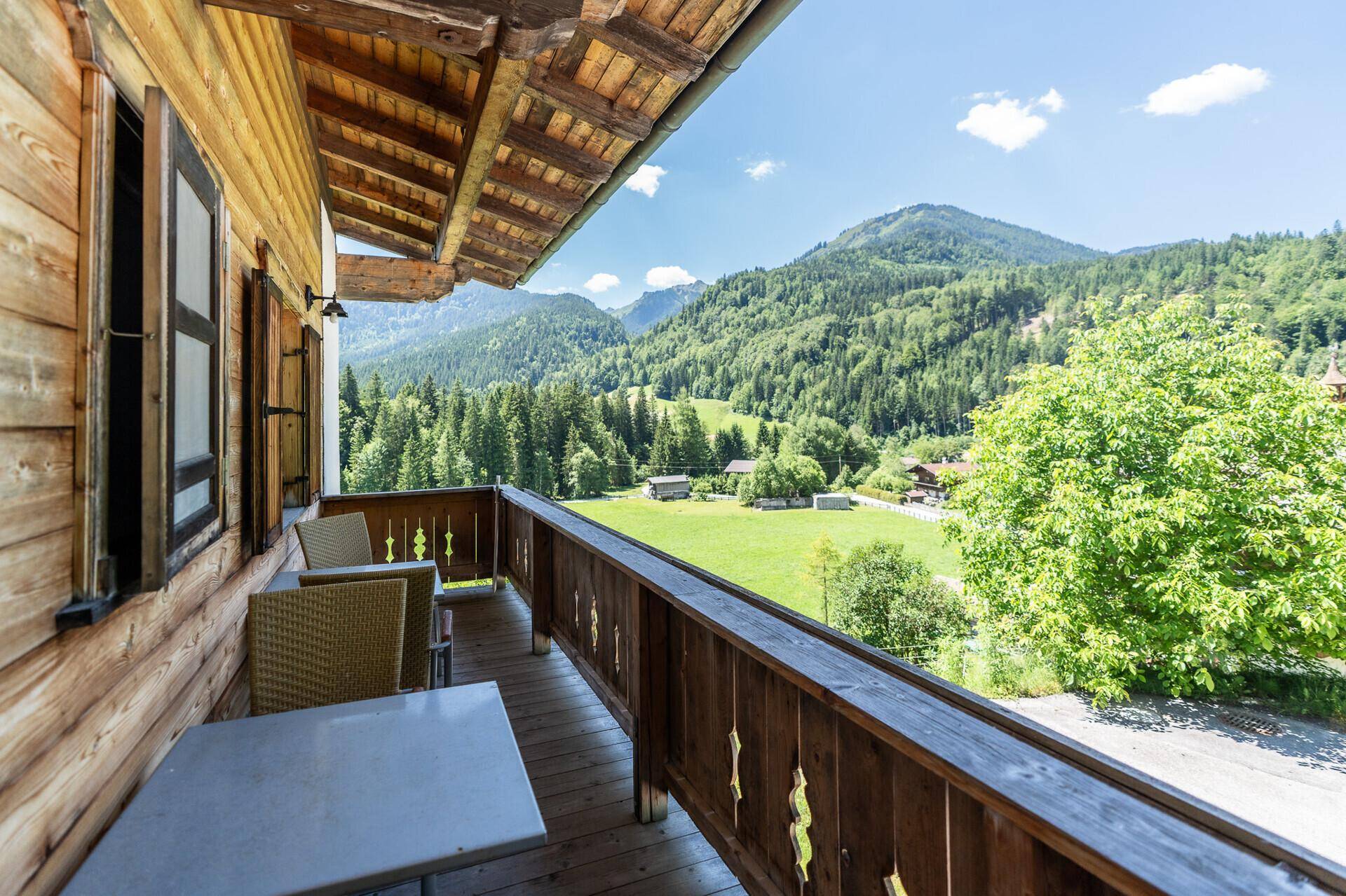 Möblierter Holzbalkon mit atemberaubendem Blick auf die umliegende Berglandschaft und grüne Wiesen.