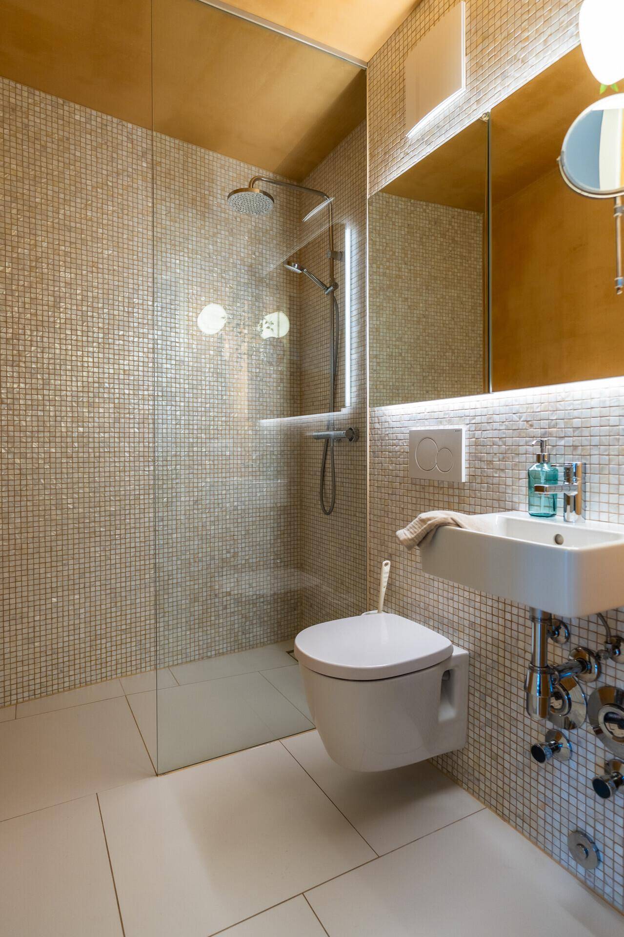 Modernes Badezimmer mit Mosaikfliesen, bodengleicher Dusche und wandhängendem WC.
