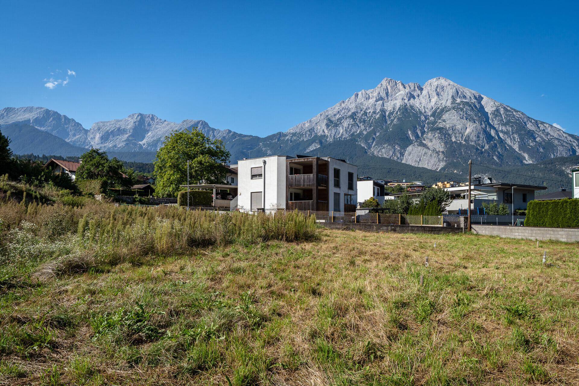 Unbebautes Grundstück mit weitem Blick auf die umliegende Wohnbebauung und die beeindruckende Berglandschaft.