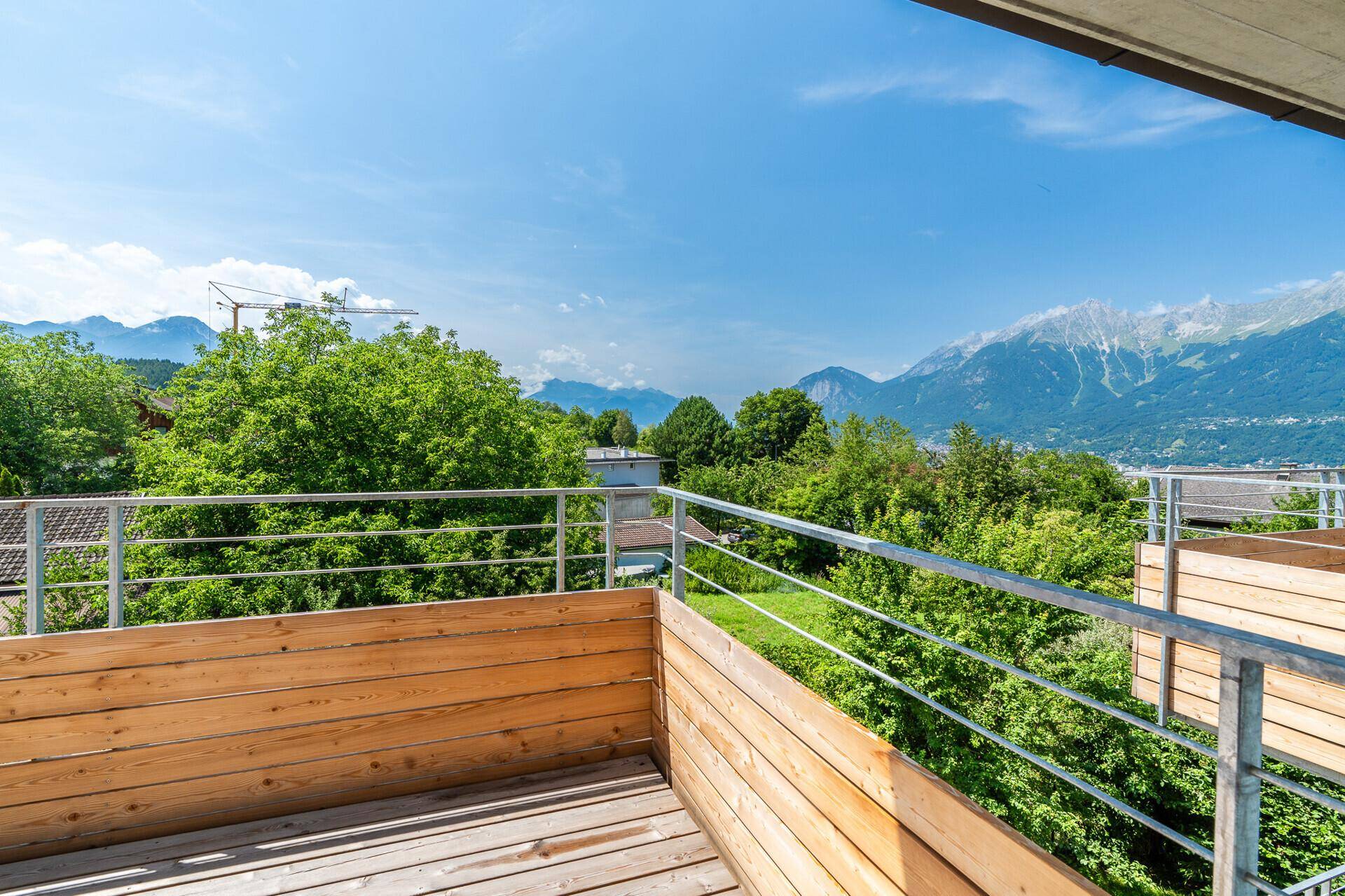 Geräumiger Holzbalkon mit Metallgeländer und weitem Blick über die grüne Landschaft und Berge.