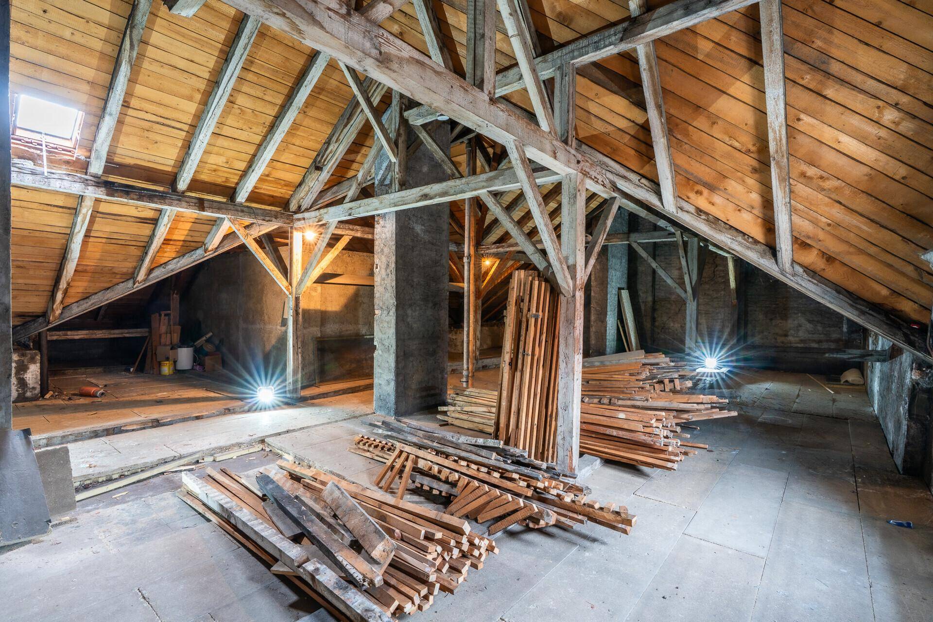 Heller Dachboden mit sichtbarer Holzkonstruktion und Baumaterialien, bereit für den Umbau.