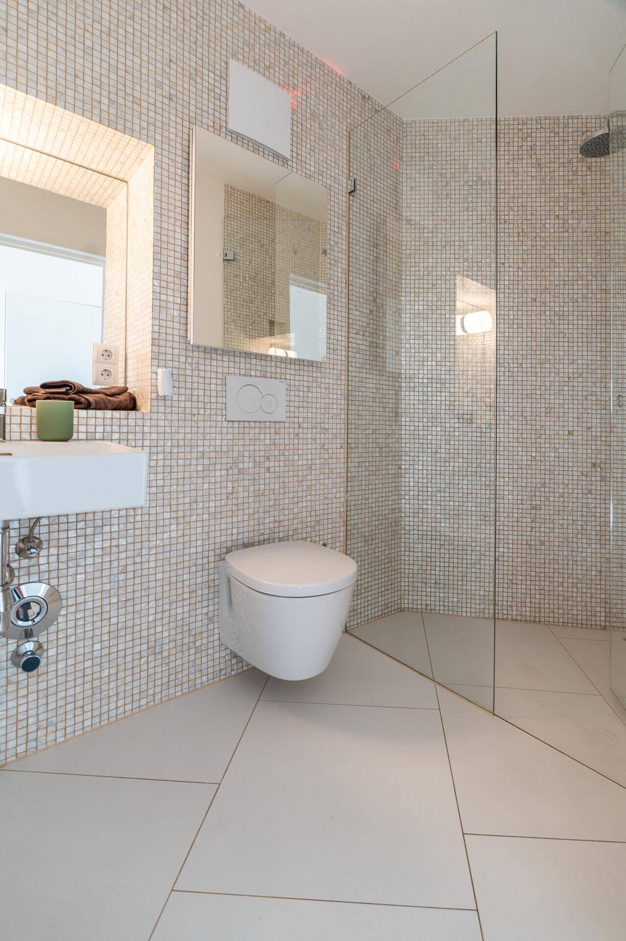 Modernes Badezimmer mit Mosaikfliesen, wandhängendem WC und begehbarer Dusche.