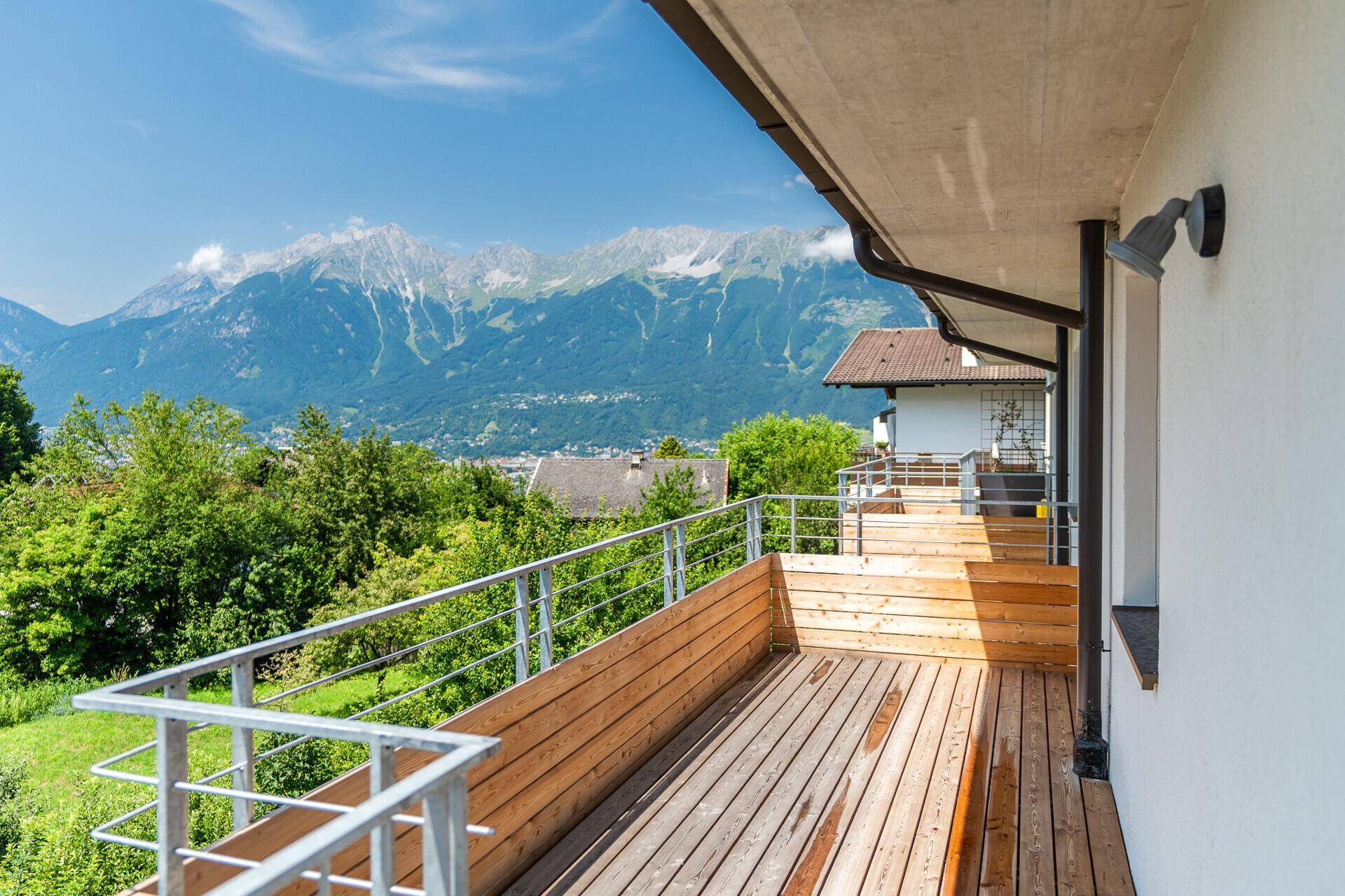 Geräumiger Holzbalkon mit atemberaubendem Bergblick und viel Grün.