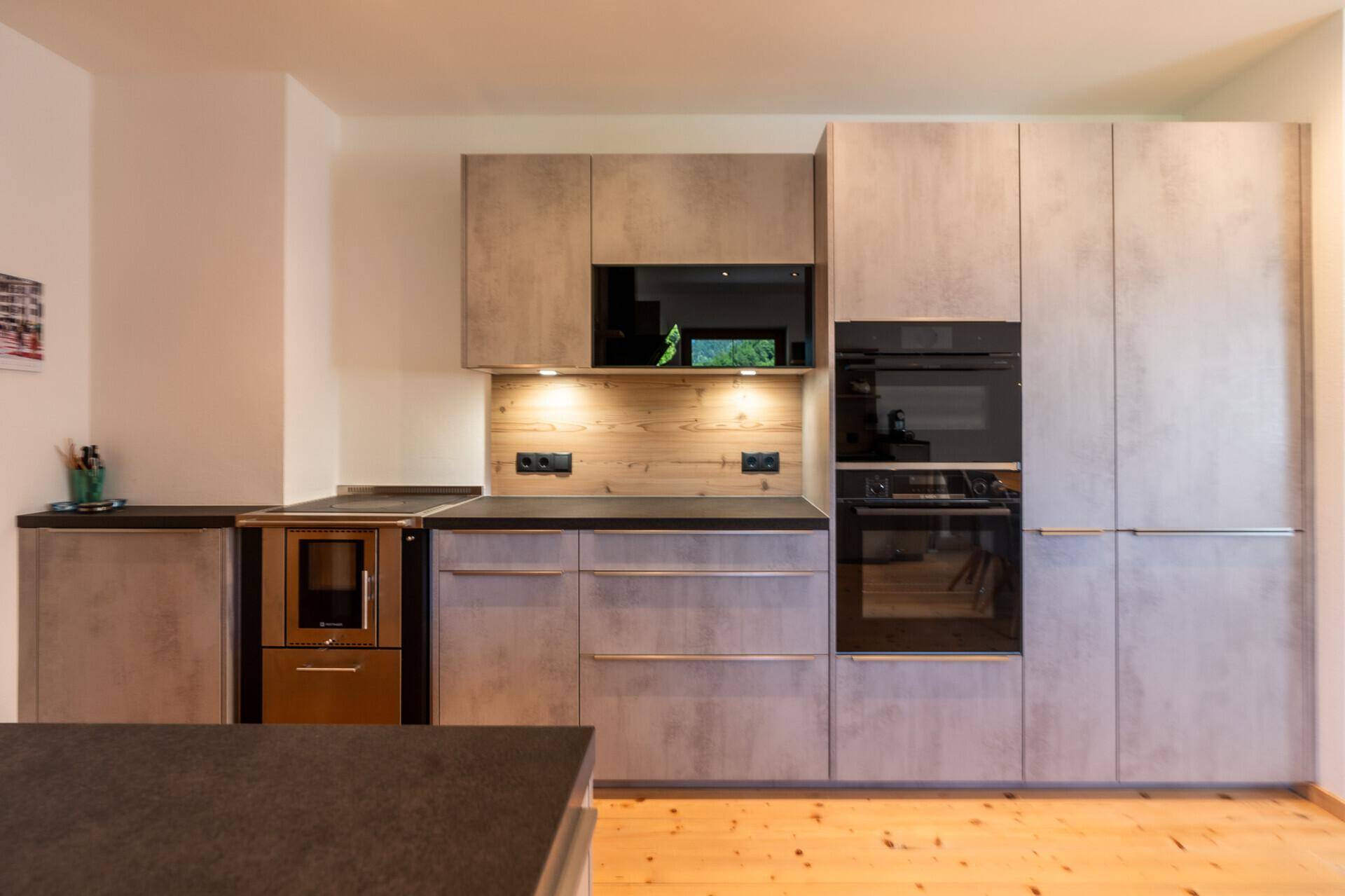 Moderne Küche mit grauen Fronten, integrierten Geräten und einer Arbeitsplatte in dunkler Optik.