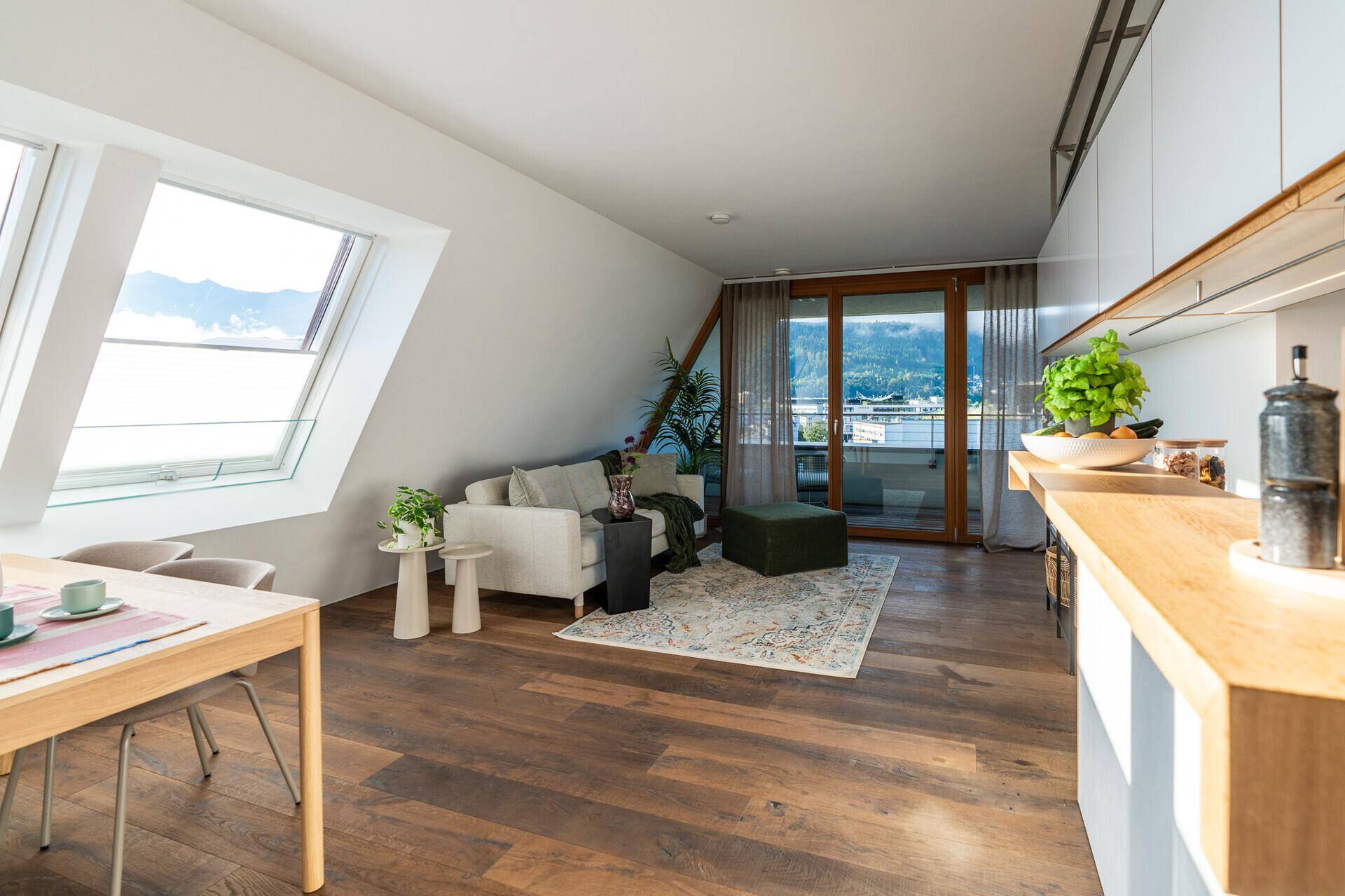 Heller offener Wohnbereich mit Küche, Essplatz und Zugang zu Balkon und Dachfenstern.