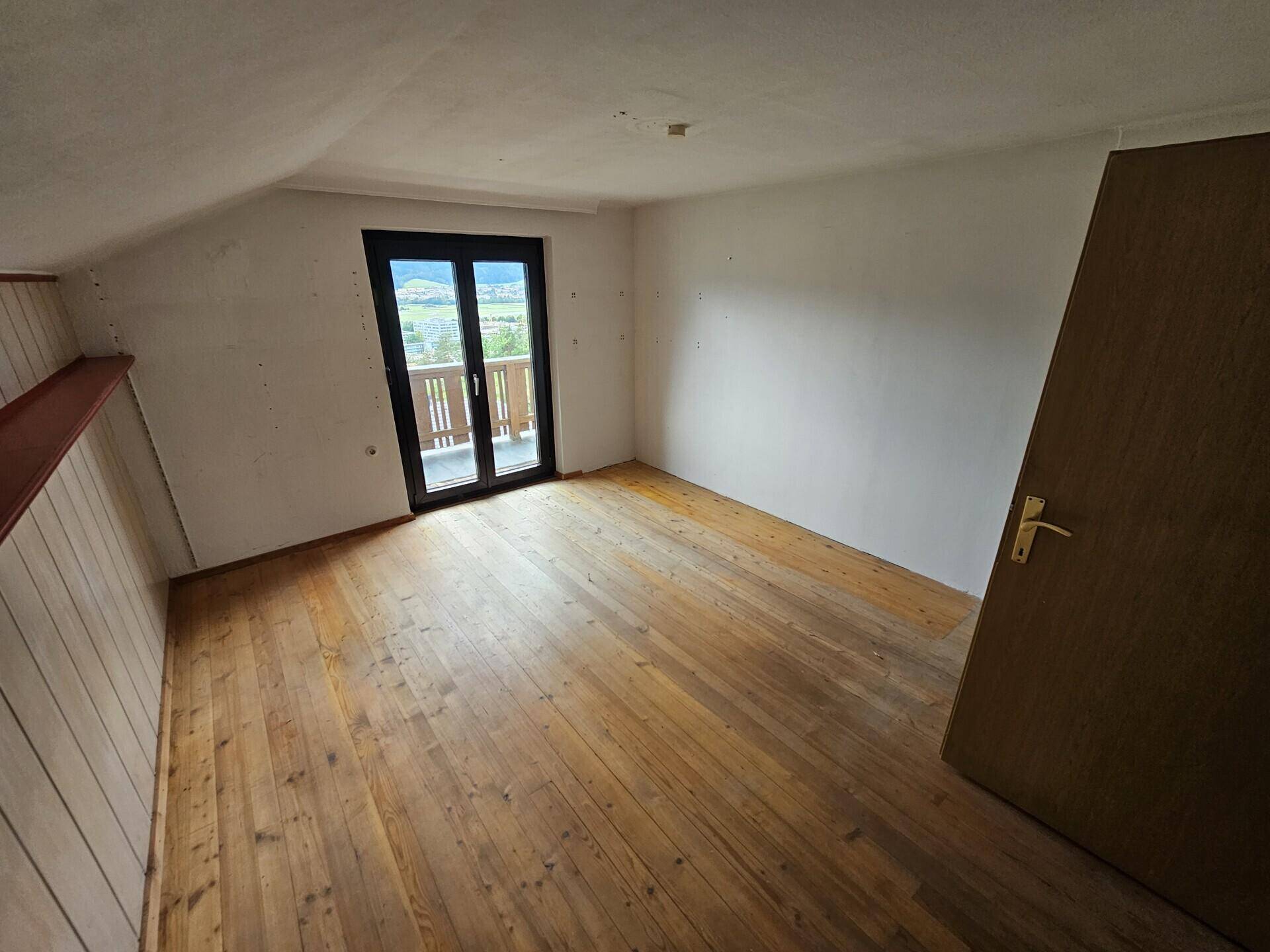 Helles Dachzimmer mit Holzboden und Zugang zu einem kleinen Balkon mit Bergblick.
