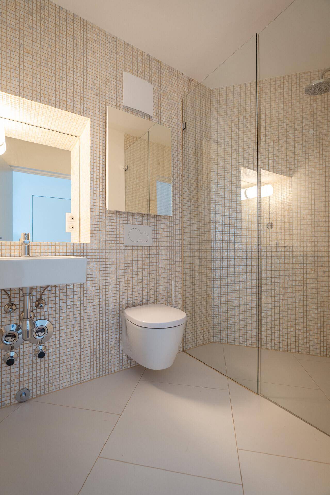 Modernes Badezimmer mit Mosaikfliesen, begehbarer Dusche und wandhängendem WC.